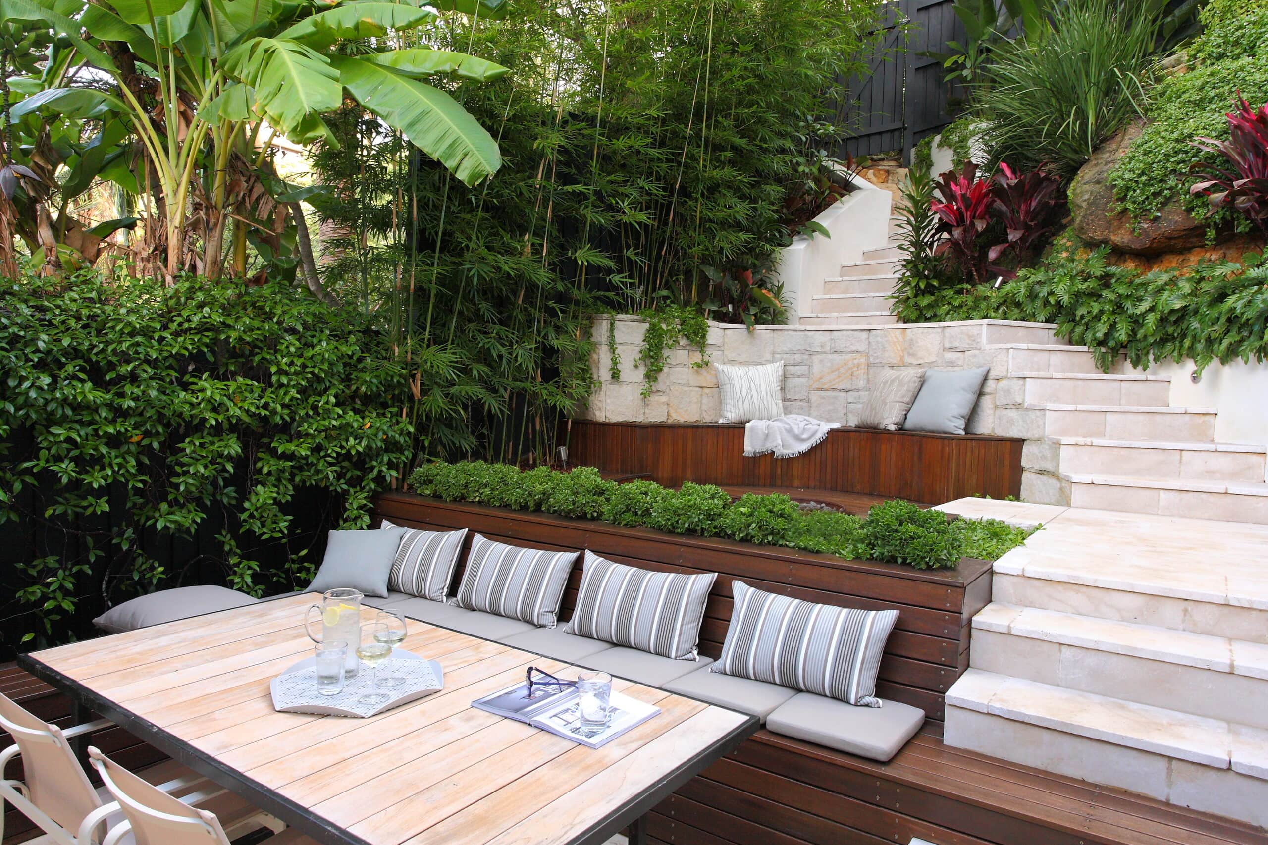Terraced tropical courtyard with timber banquette striped cushions and sandstone steps framed by bamboo and banana palms