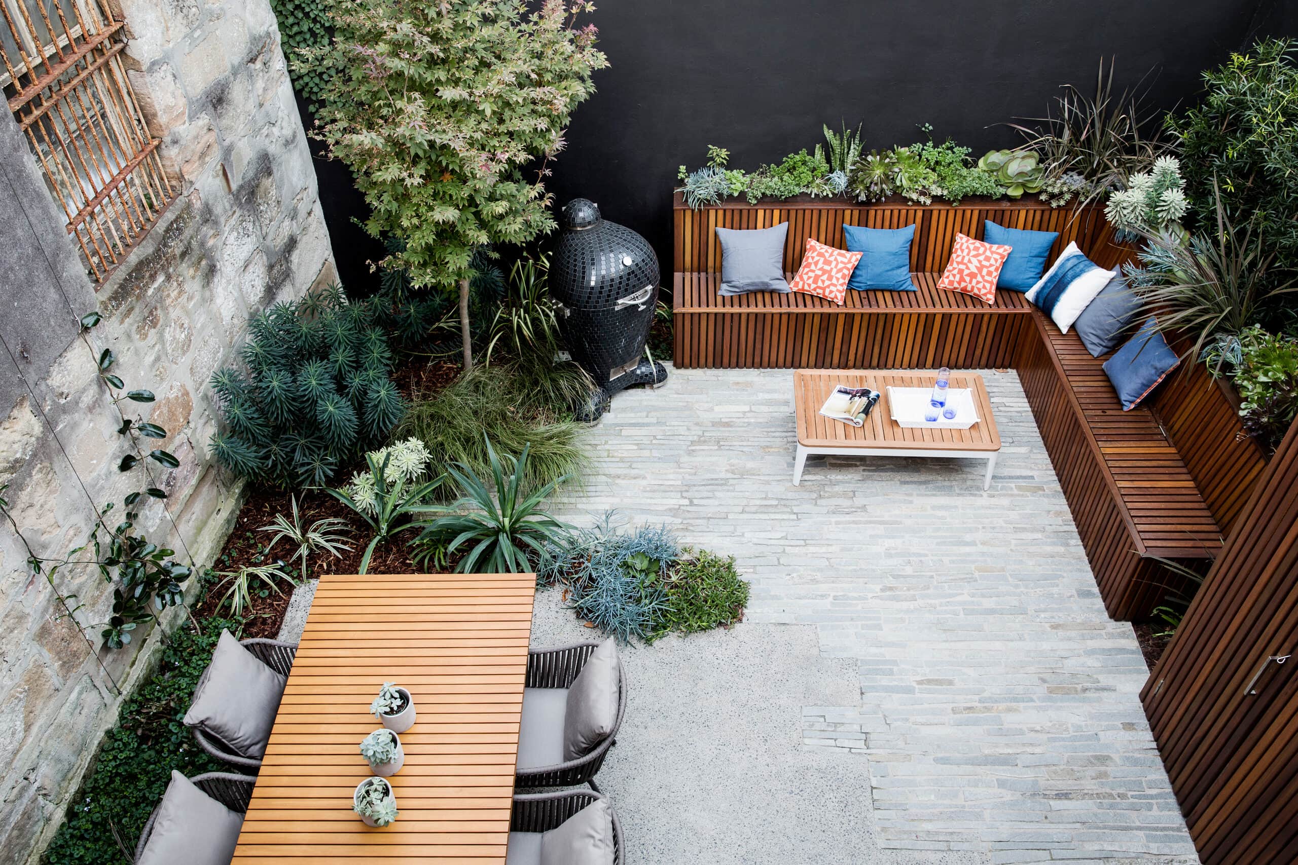 Overhead view of a compact courtyard with timber dining table sandstone wall and slatted bench seating