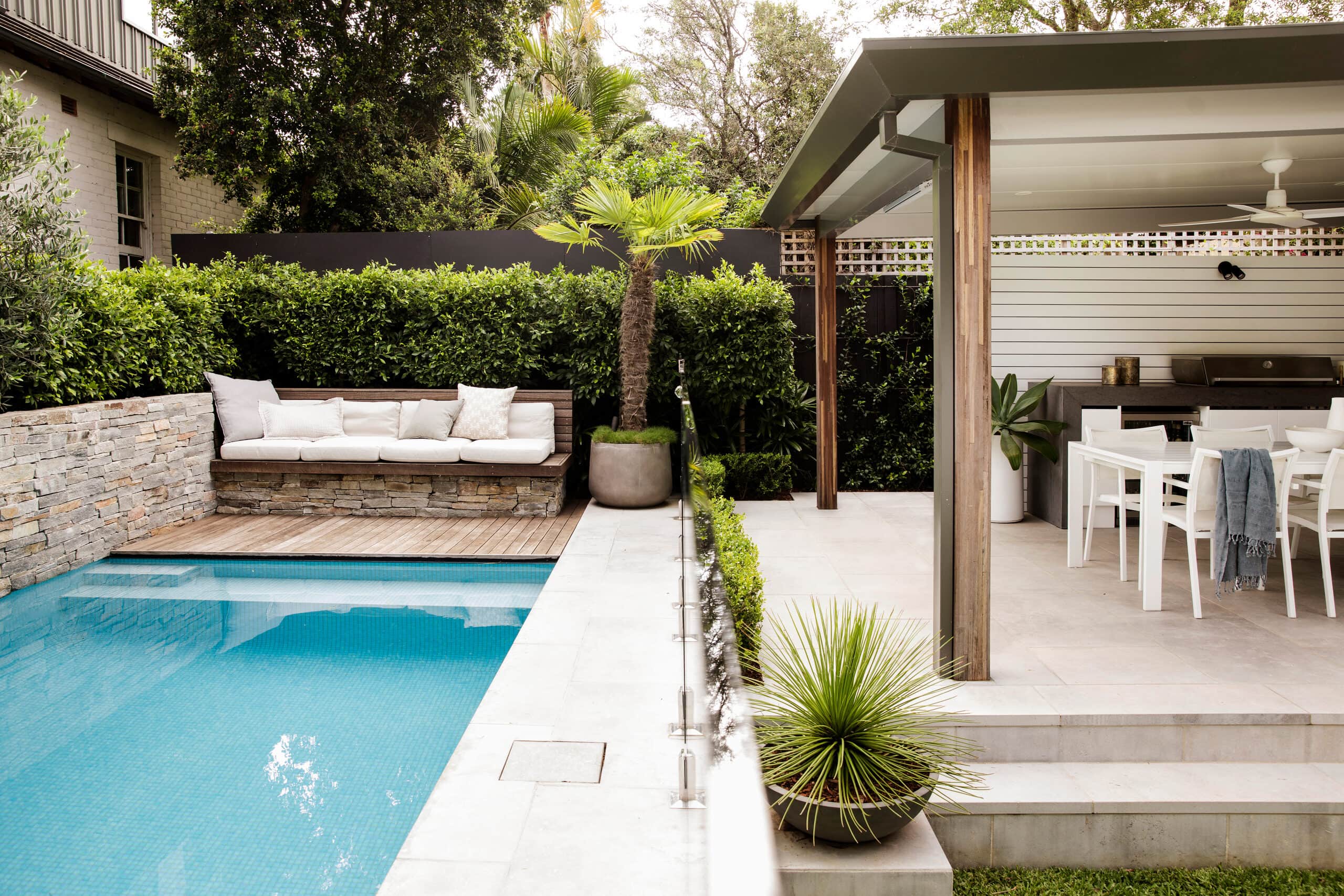 Elevated view across the mosaic pool to a stone-clad daybed and covered alfresco dining beyond