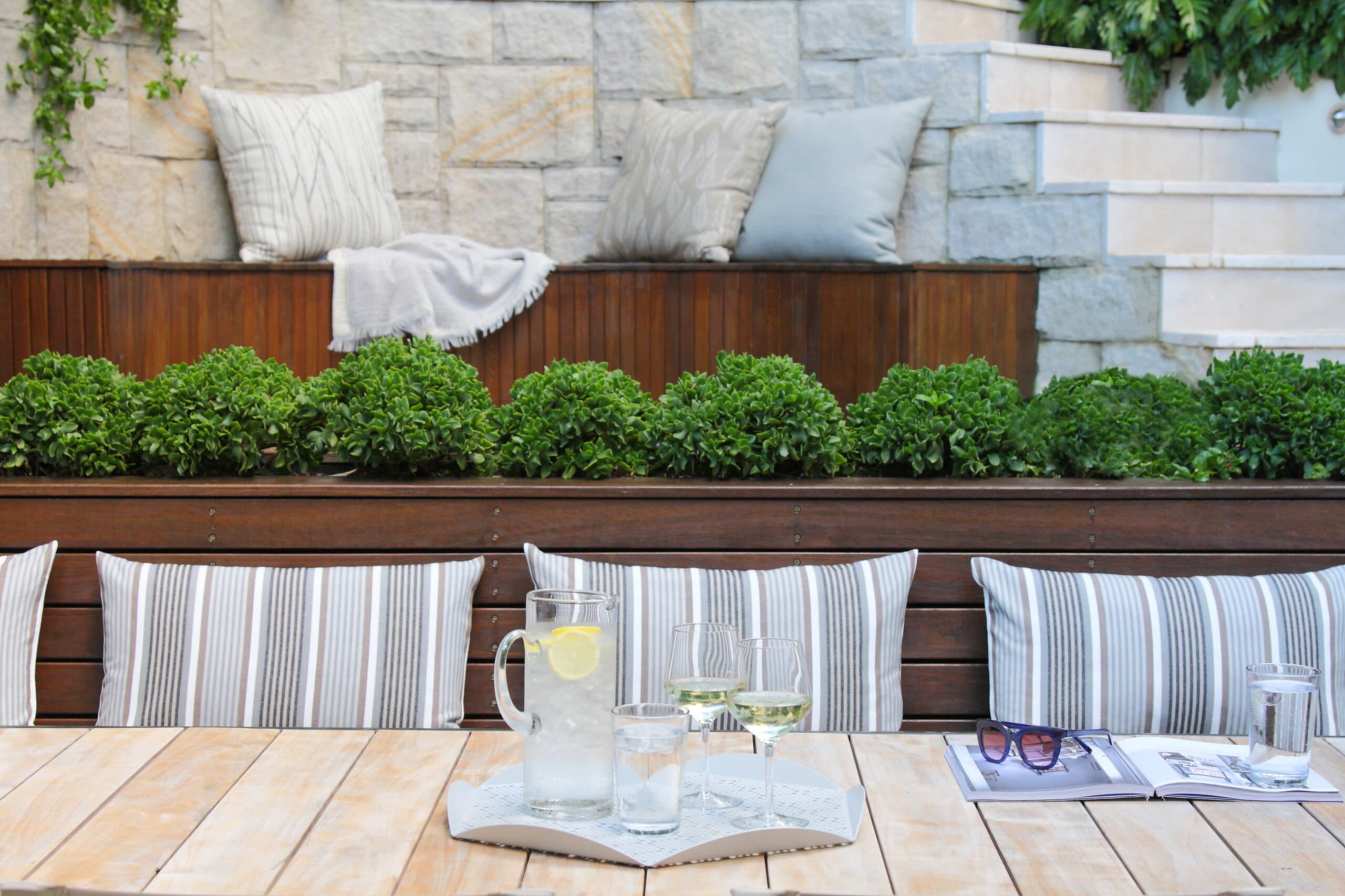 Jade succulents in a timber planter above striped seat cushions with a drinks tray on a teak table