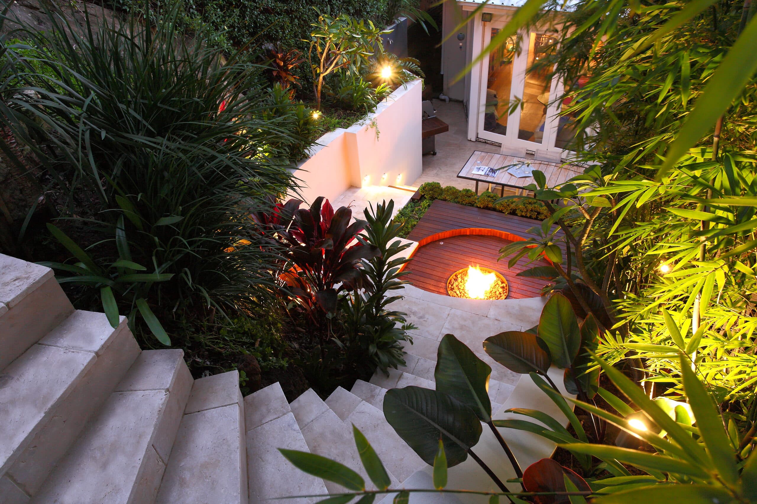Aerial evening view down stone steps into the courtyard toward a lit fire pit and glowing french doors