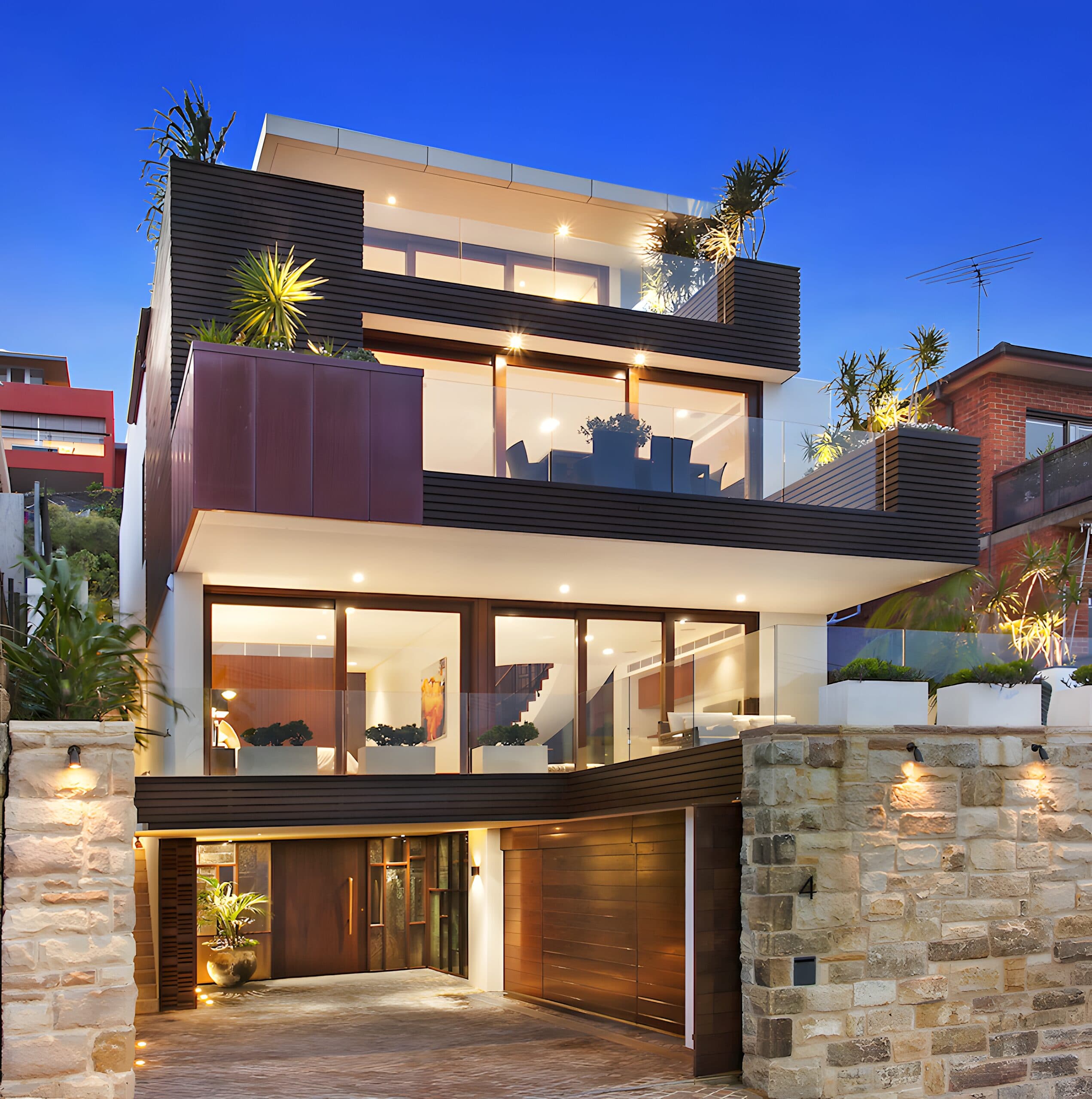 Three-storey coastal facade at dusk with sandstone gateposts and timber garage under a deep blue sky