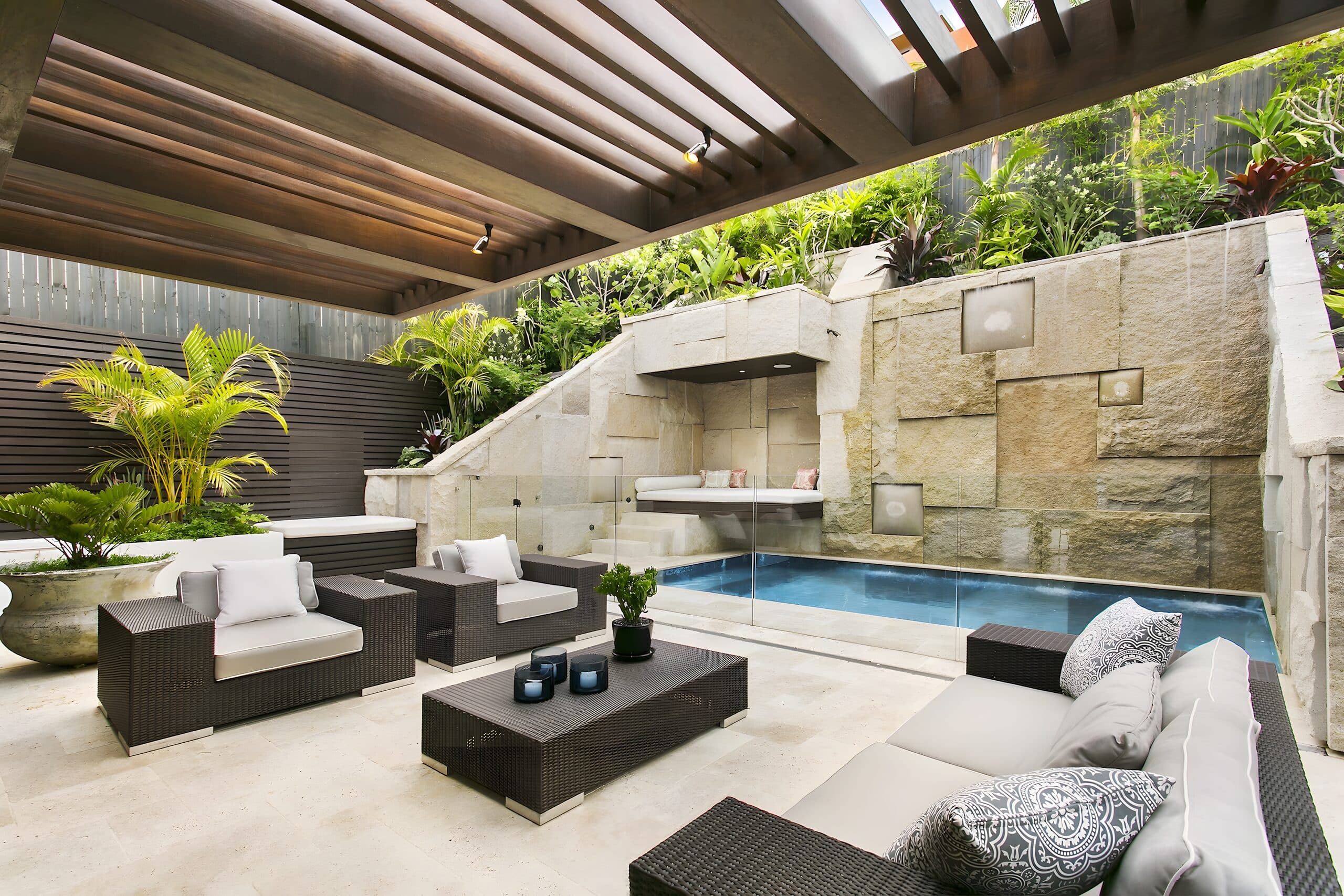 Timber pergola shading a paved lounge and plunge pool set into a carved sandstone wall
