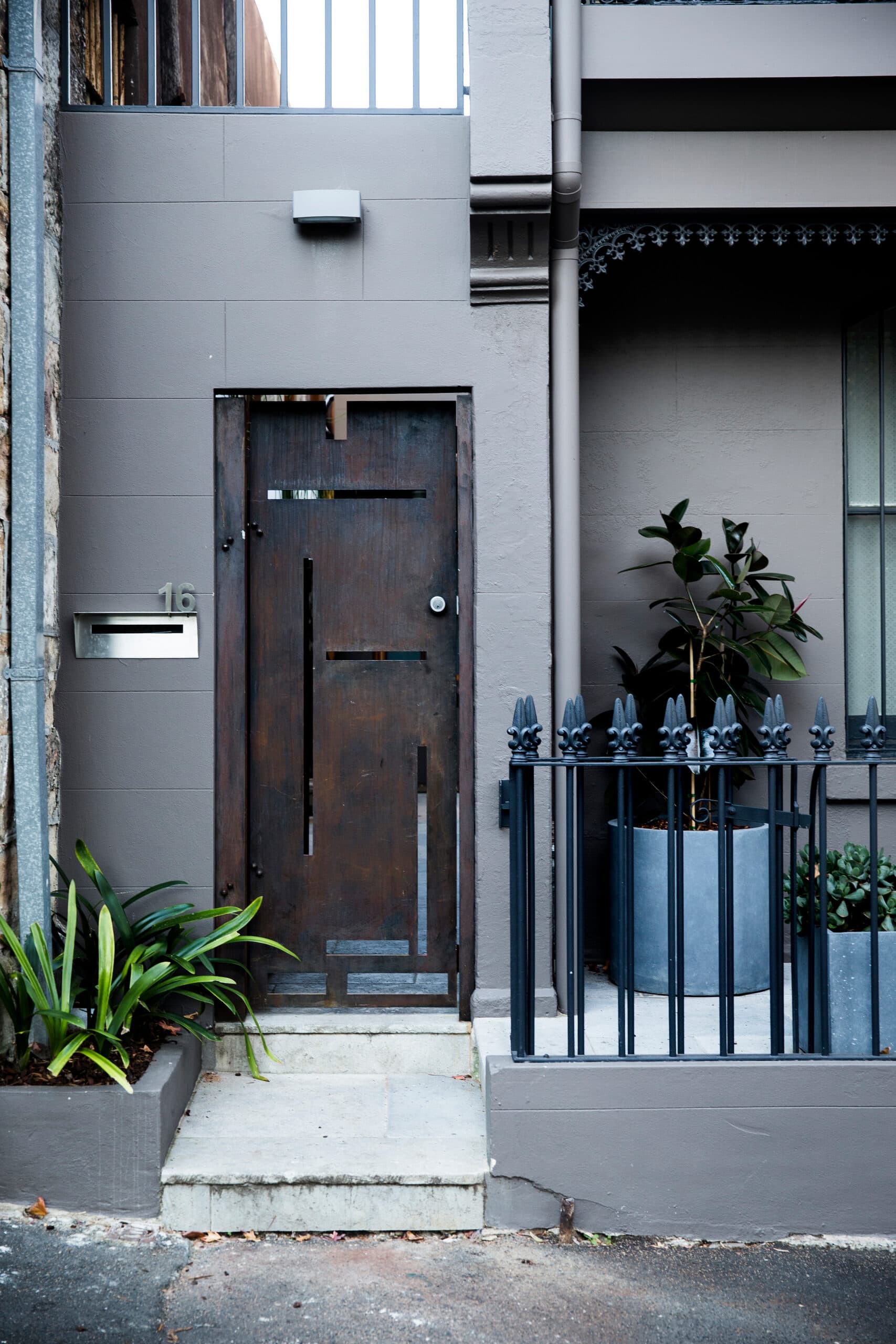 Dark timber front door of a grey terrace with potted greenery and iron railing