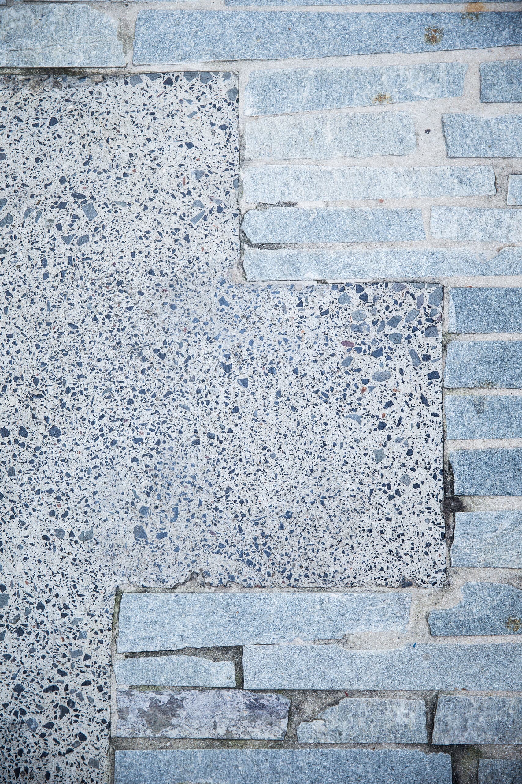 Detail of speckled terrazzo pavers meeting rough split stone paving