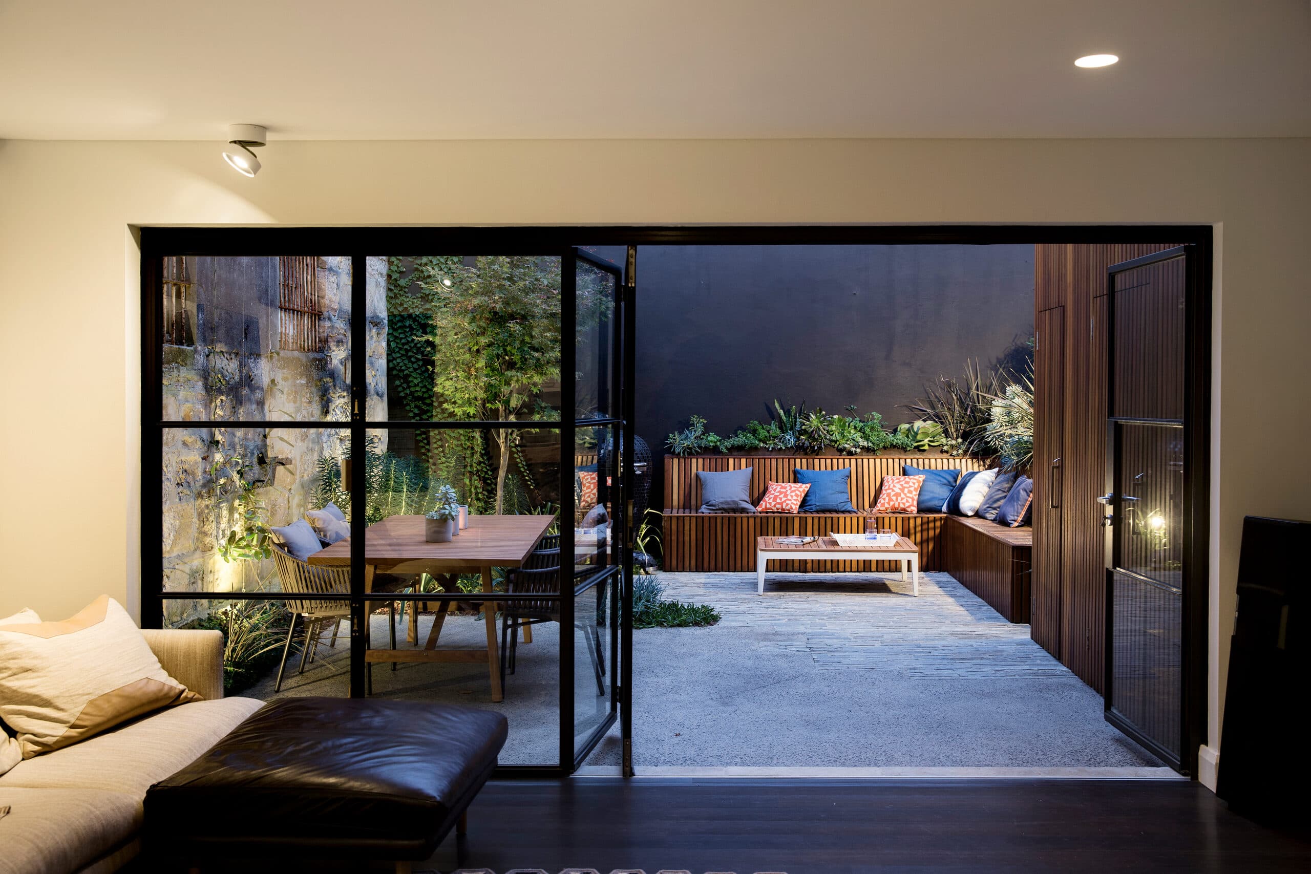 Courtyard glowing at dusk through open steel doors with lounge seating