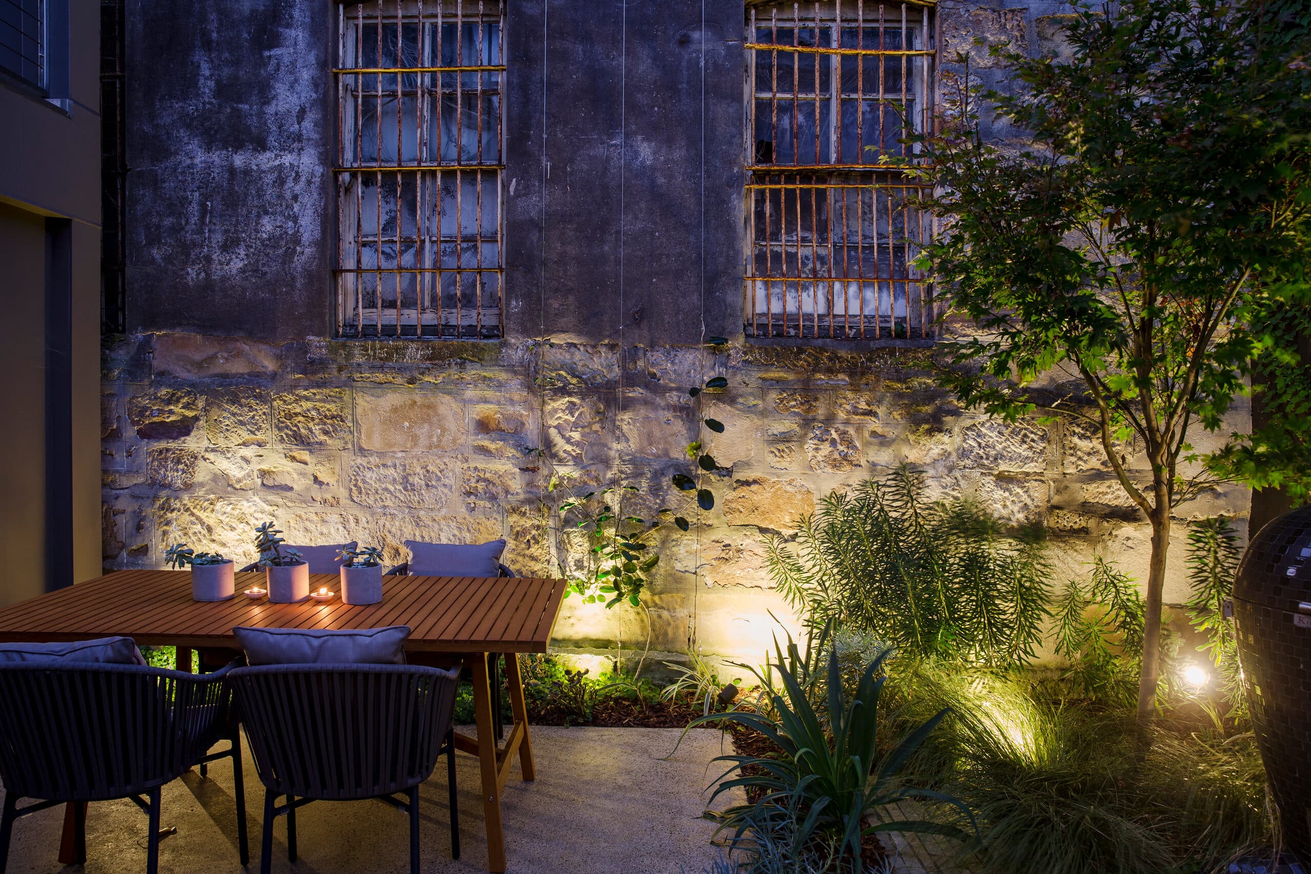 Dining table lit beneath heritage barred windows and glowing sandstone at night