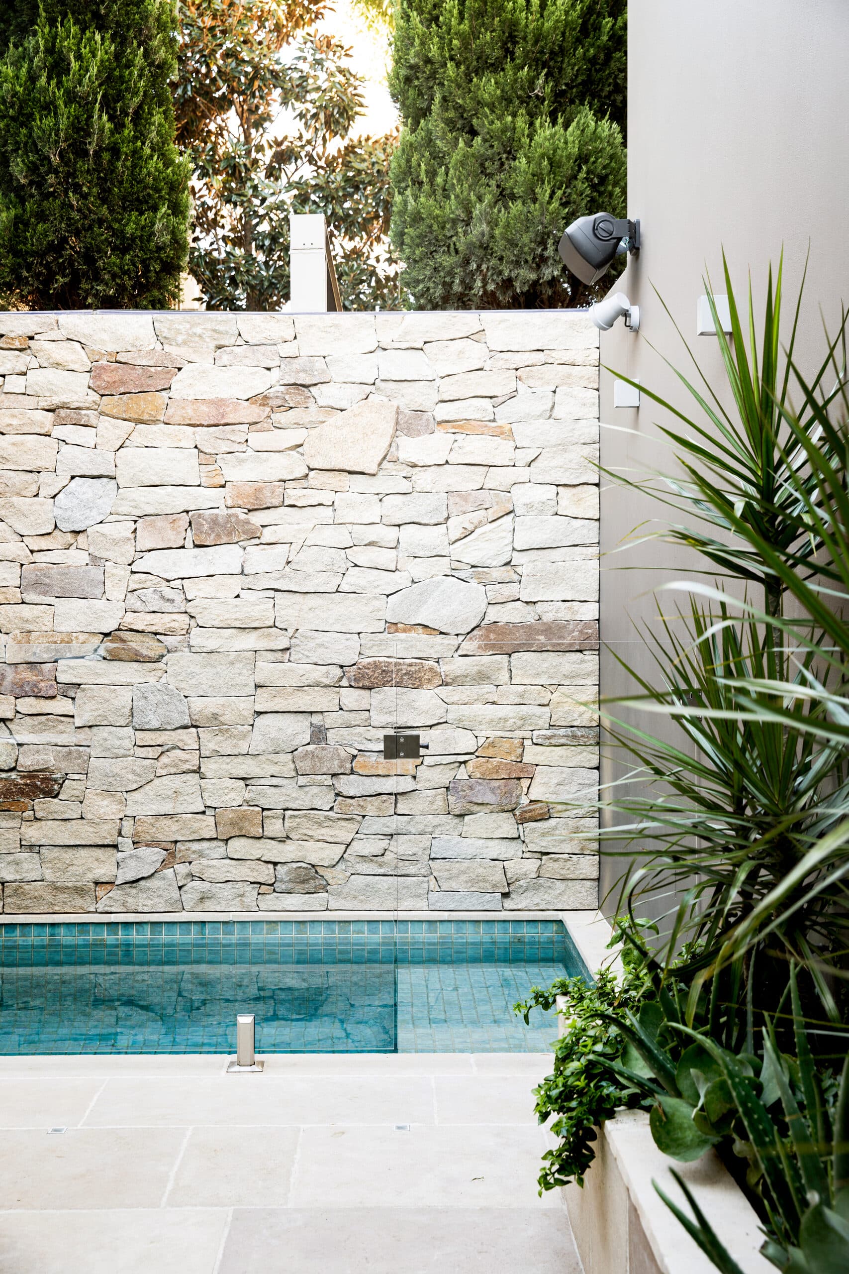 Sandstone feature wall meeting a blue mosaic plunge pool behind a frameless glass fence