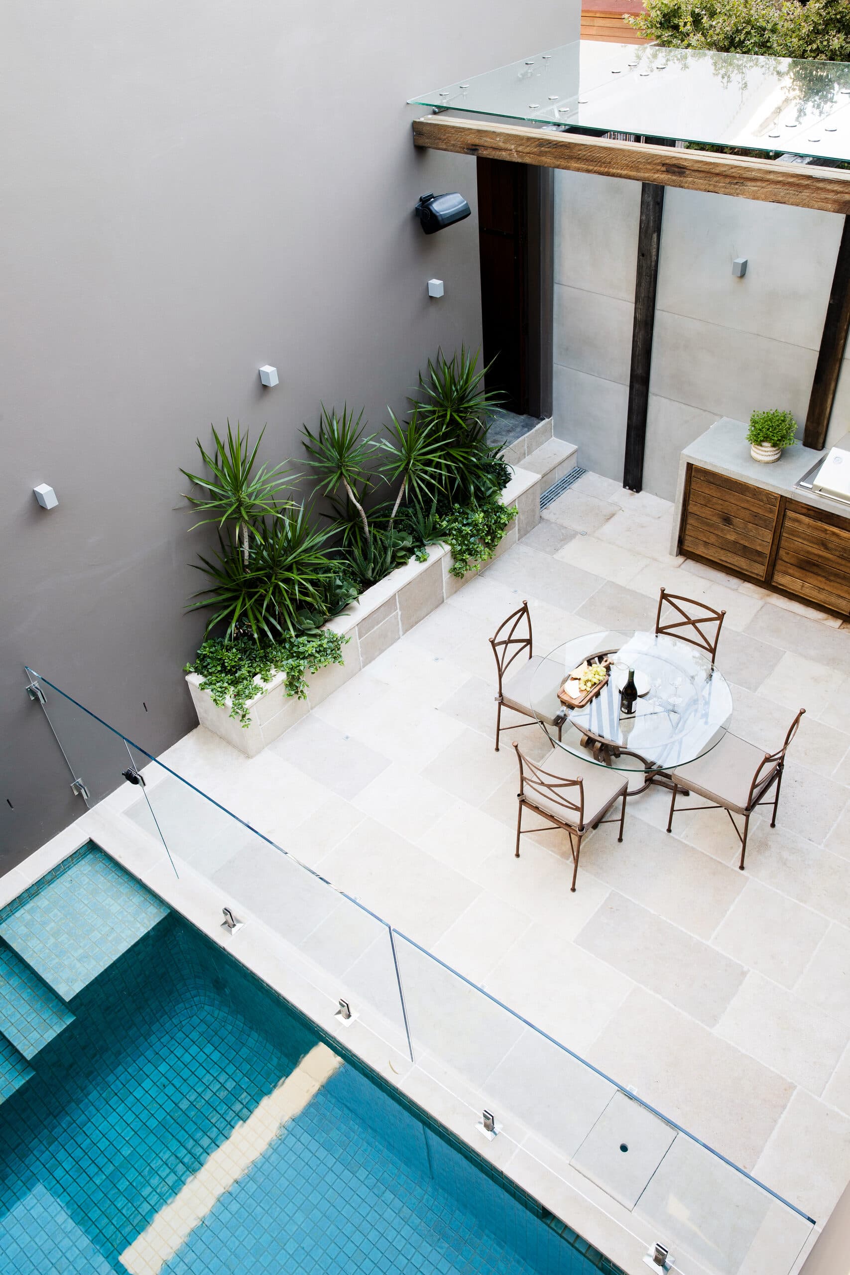 Overhead courtyard with dracaena in a sandstone planter and a glass dining table on limestone paving