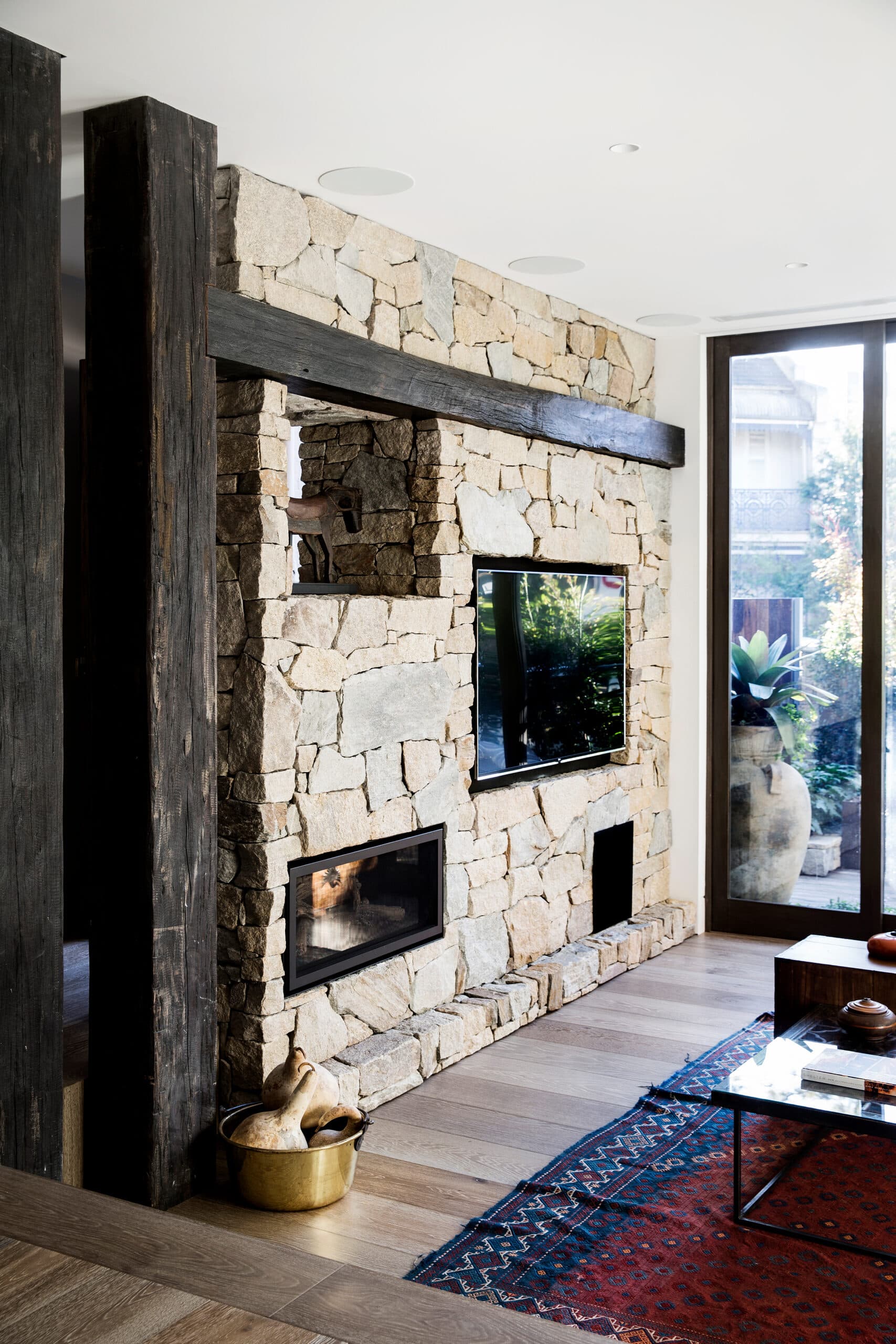 Interior sandstone fireplace wall with a mounted screen and reclaimed timber post