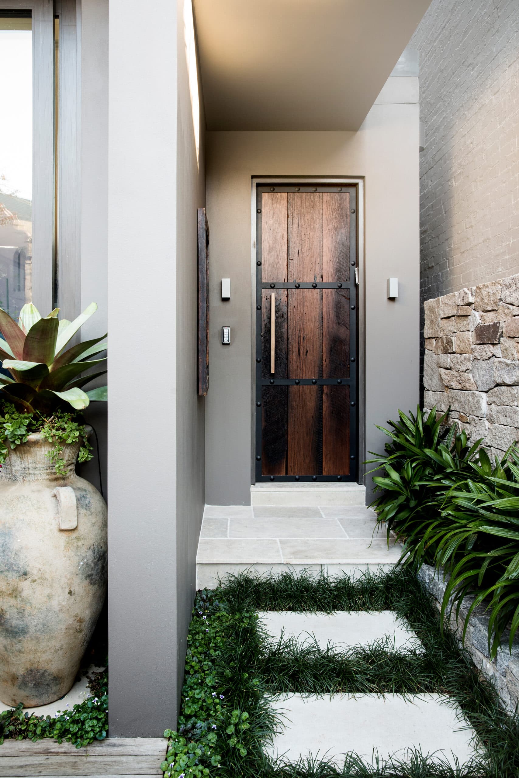 Studded dark timber entry door with sandstone steps and a grass and paver path