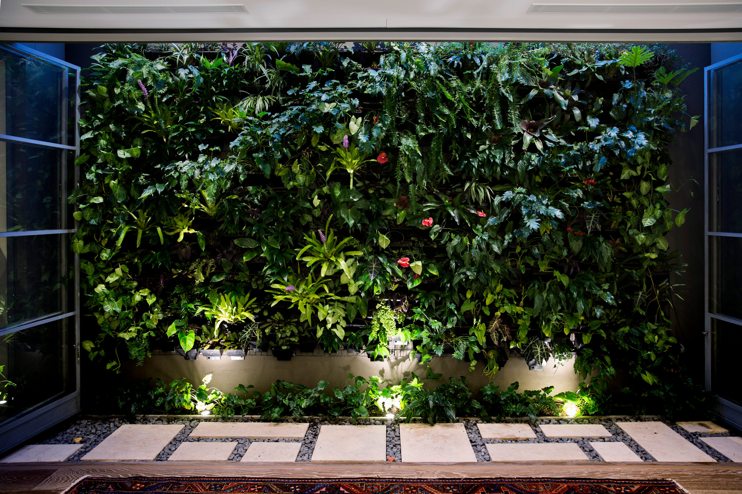 Illuminated living wall at night above a paver path and layered rug