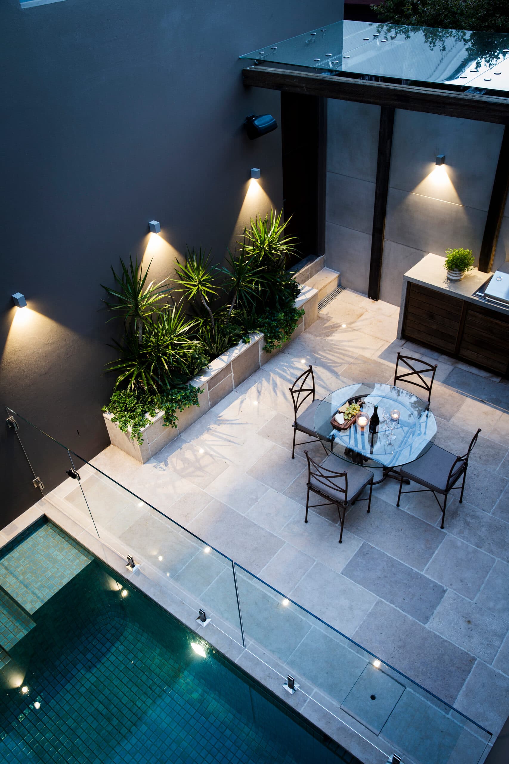 Courtyard from above at dusk with uplit walls and a candlelit glass dining table