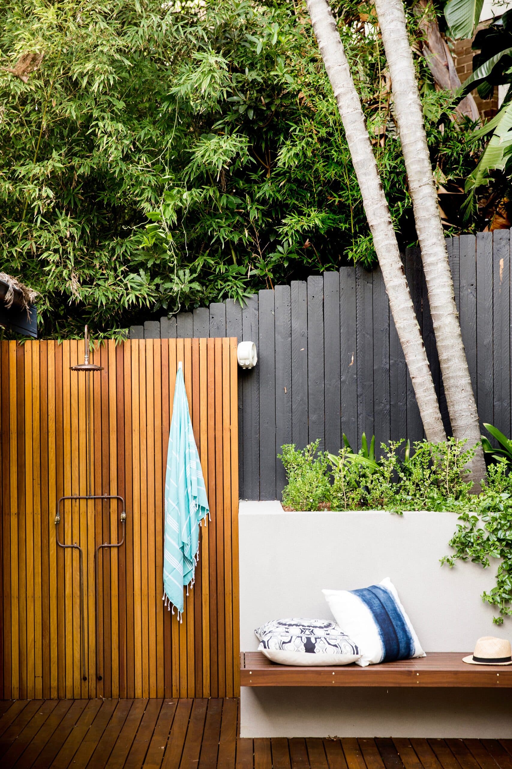 Timber slat outdoor shower with a turquoise towel beside a built in bench under tall palms