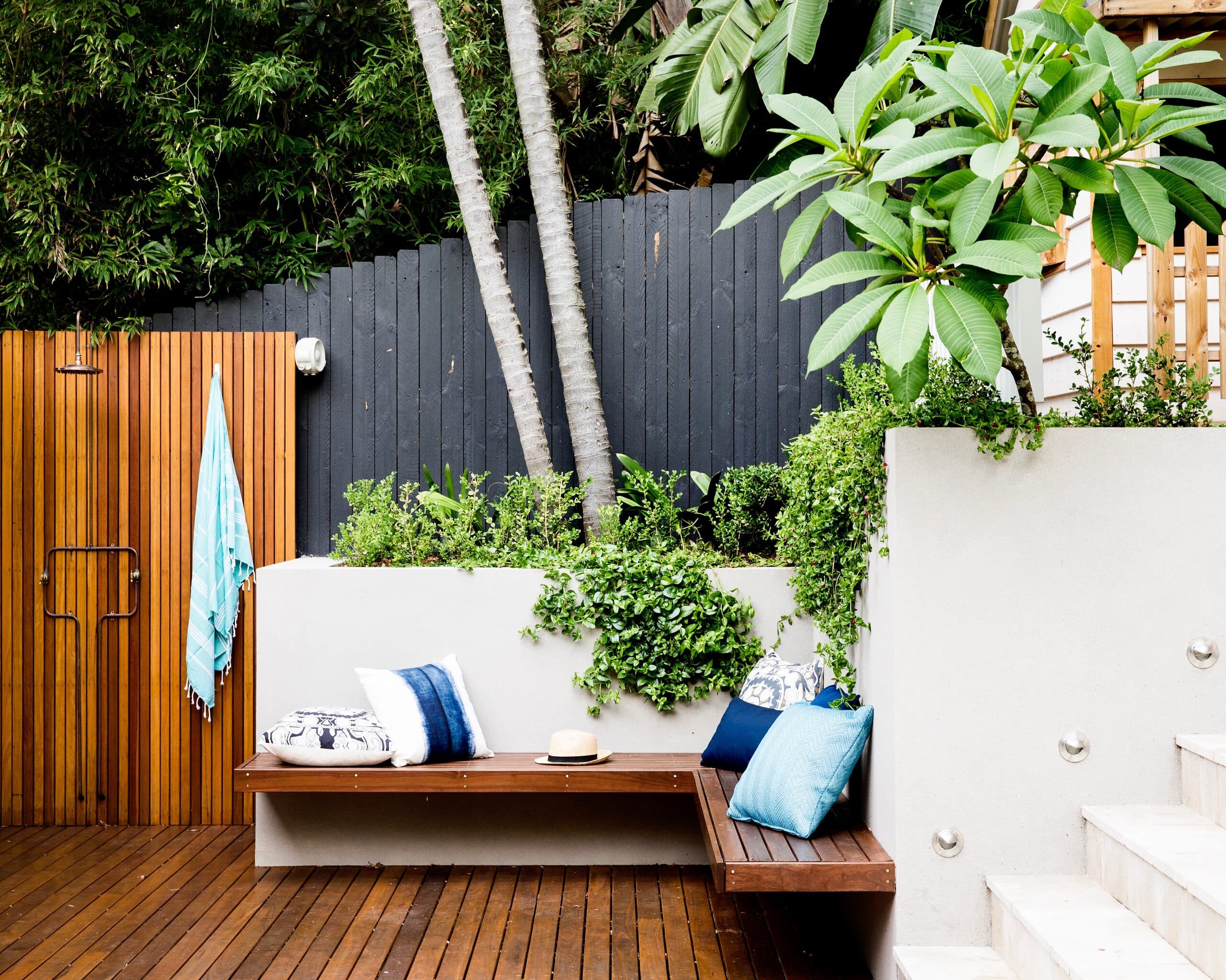 Corner bench with blue and white cushions against a rendered planter wall trailing ivy beside sandstone steps