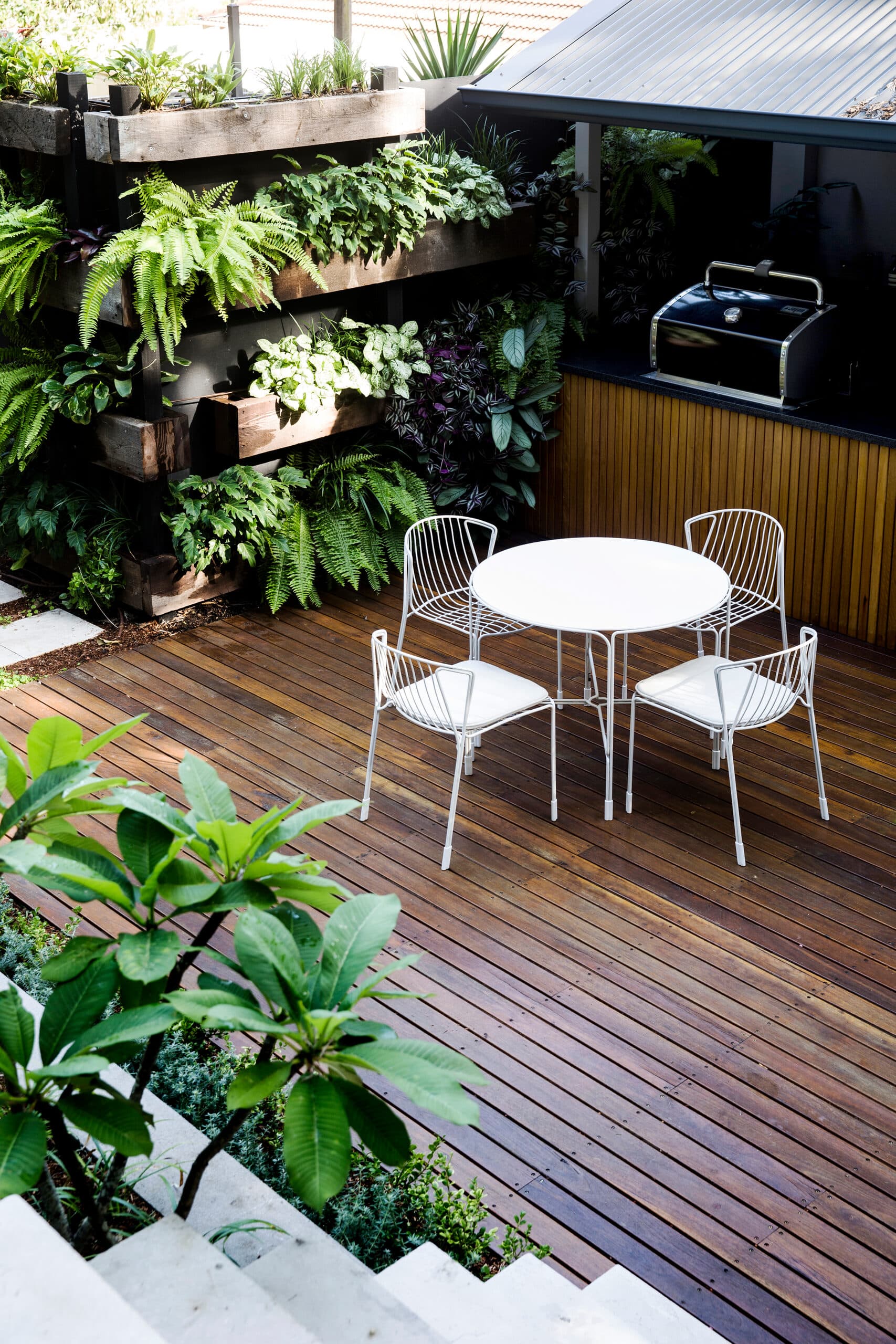 Looking down on white wire dining set on timber decking beside a living wall and barbecue kitchen