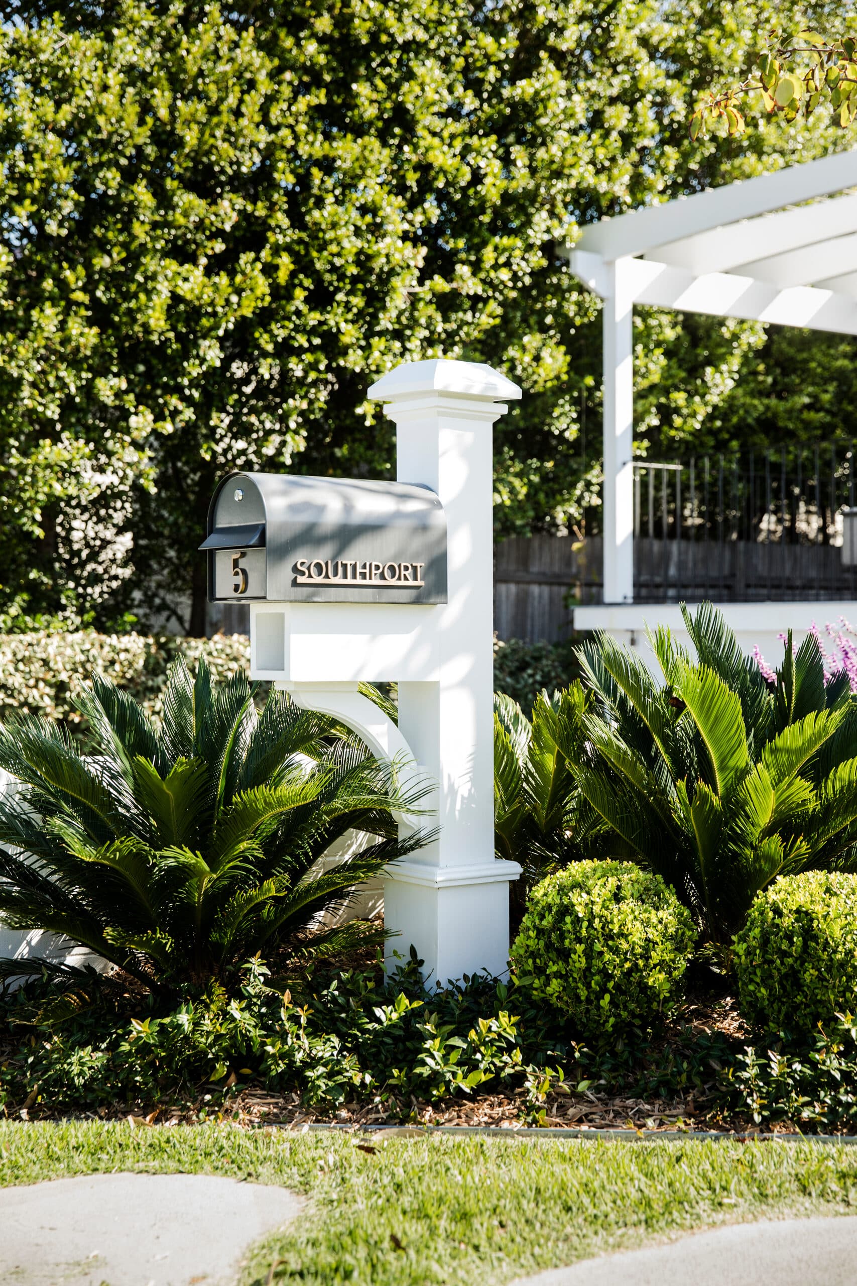 White timber mailbox post reading Southport beside cycad palms and clipped hedging