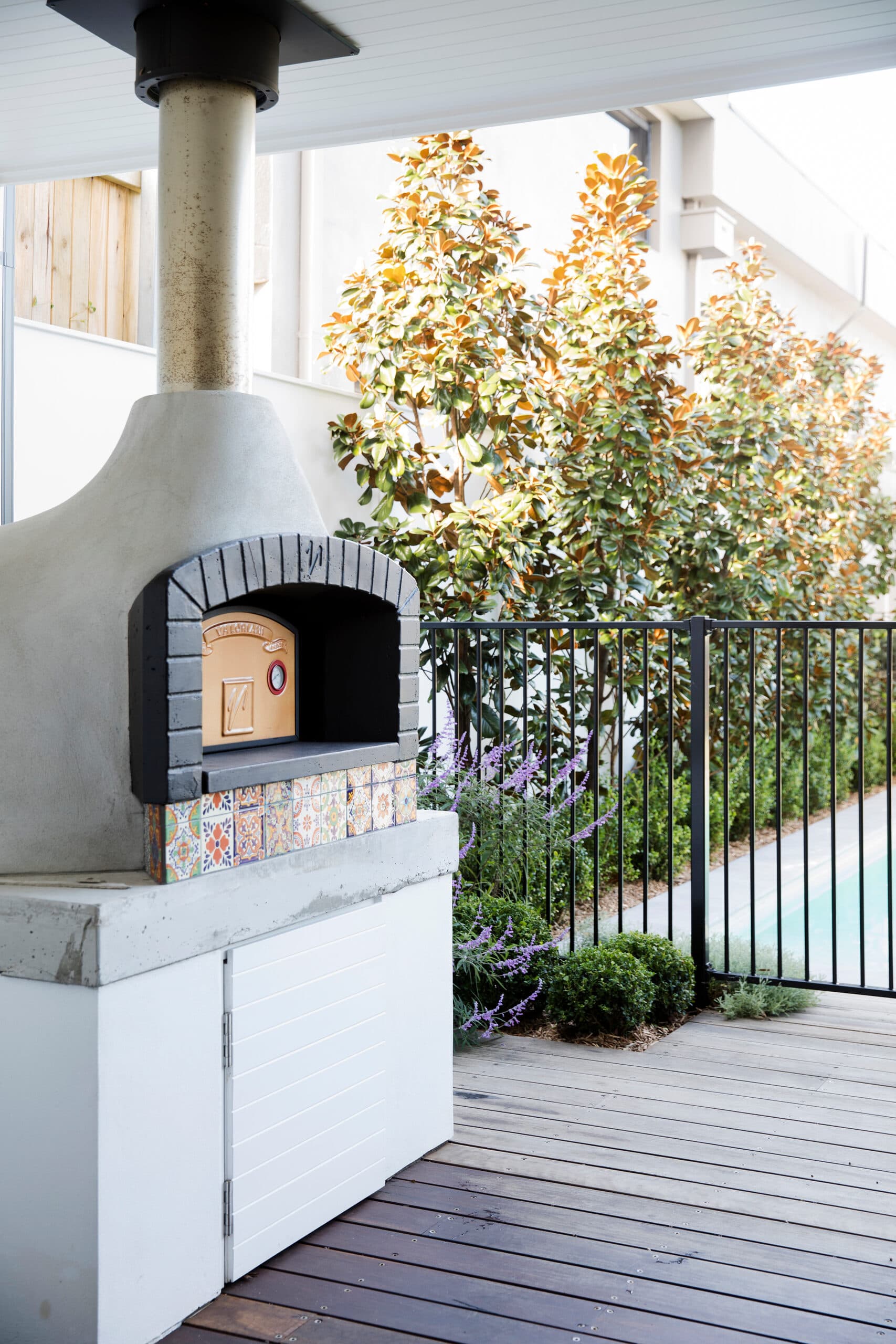 Concrete wood fired pizza oven with tiled front beside salvia and a pool fence
