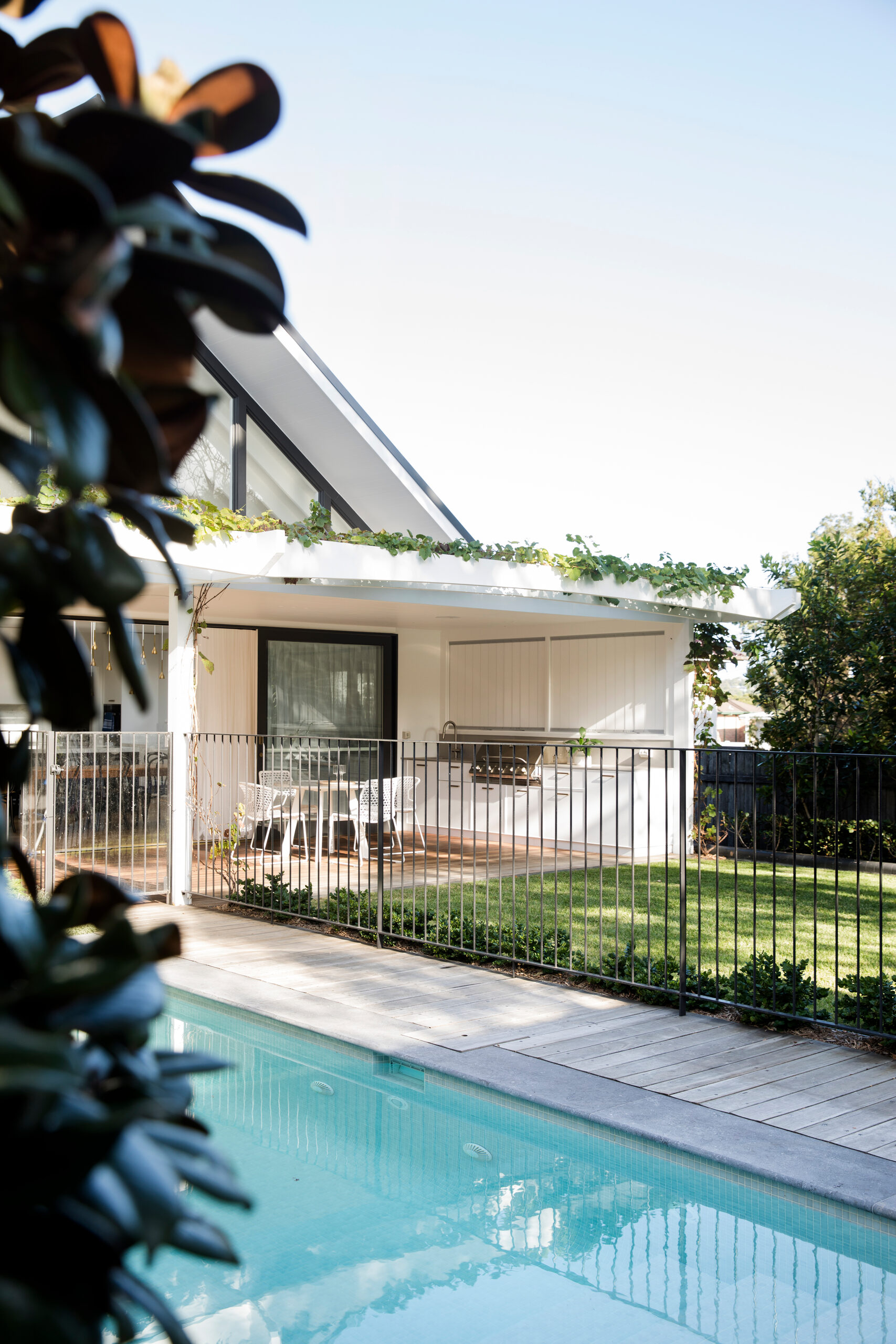 Tiled pool and timber deck looking to a covered verandah behind a black pool fence