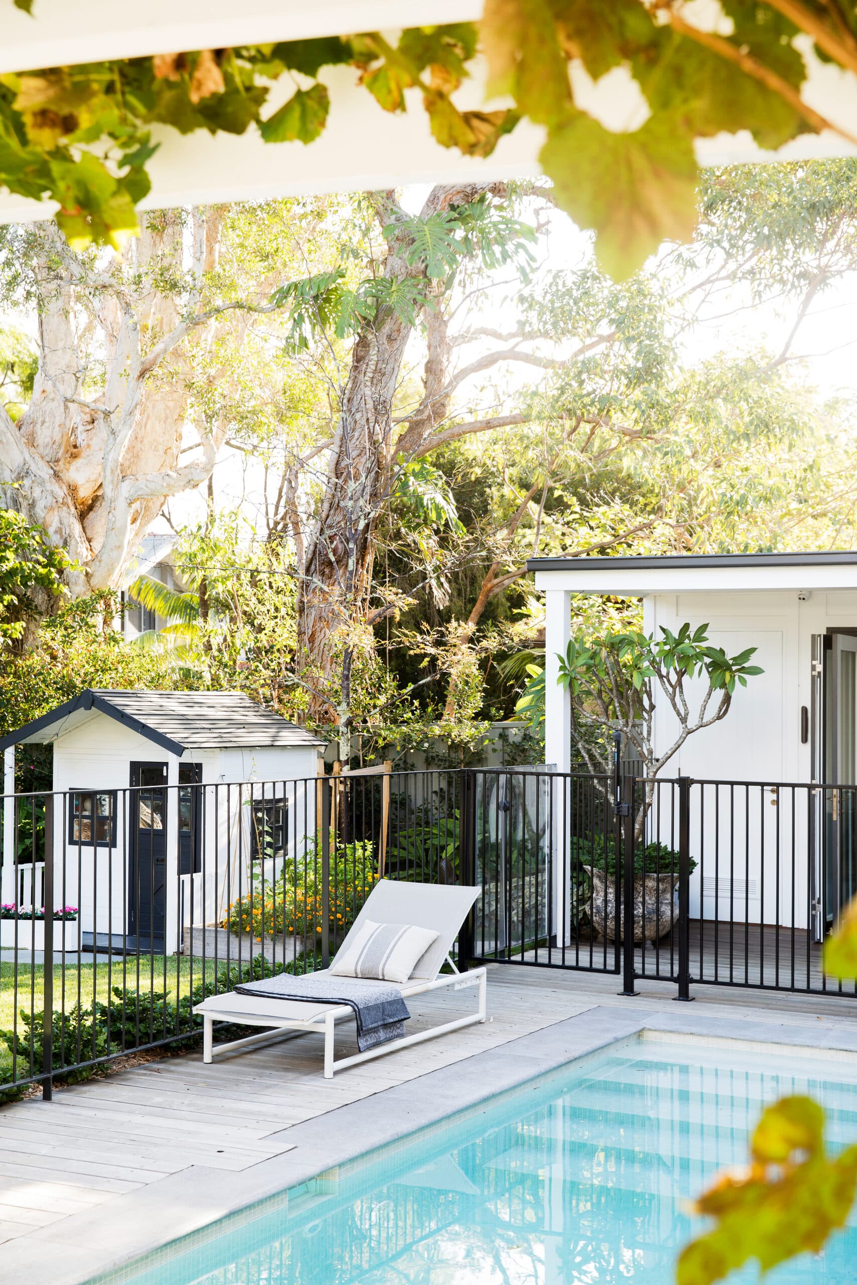 White sun lounger on the deck by the pool with black cabana and leafy backdrop