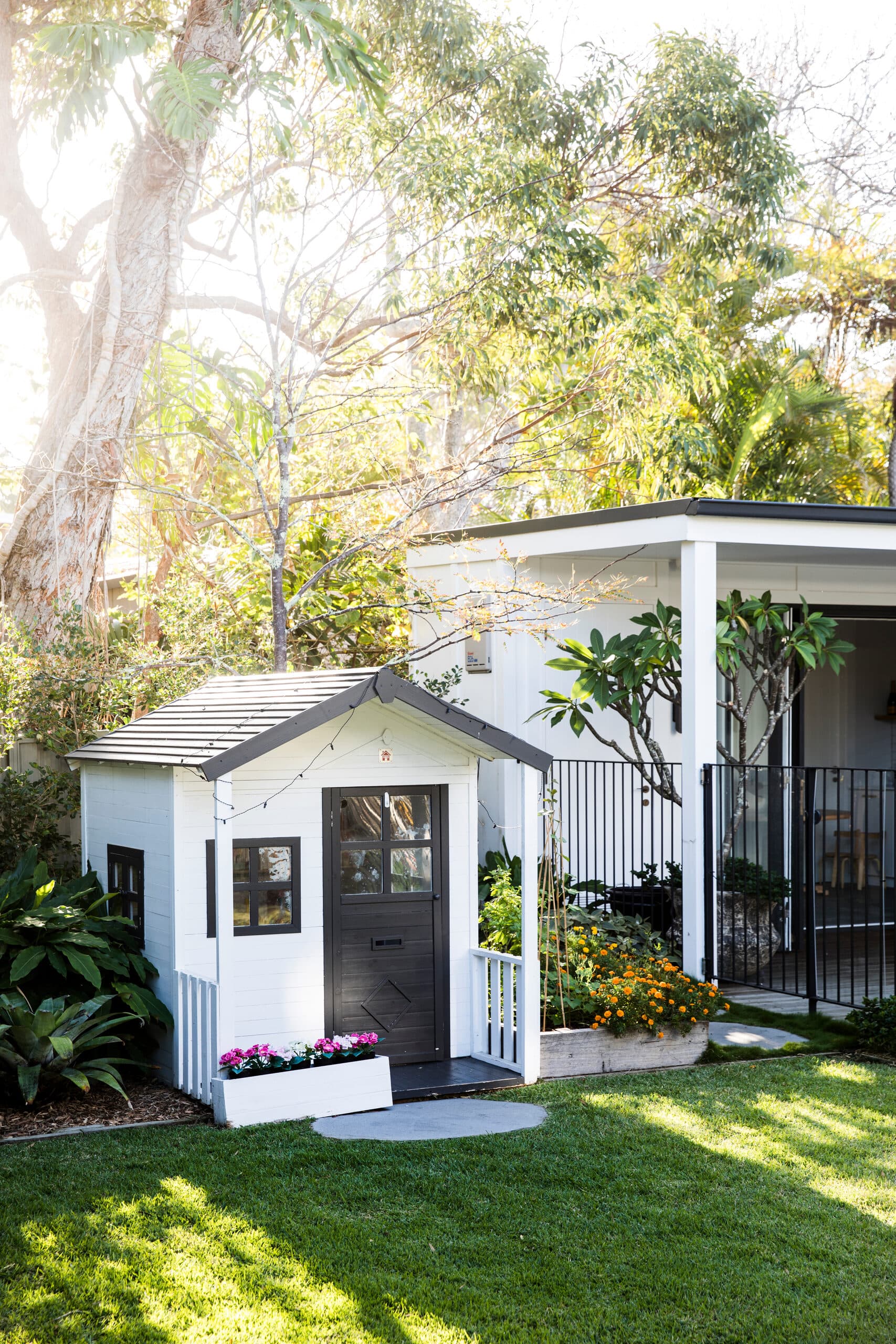 Childrens cubby house in white and black beside marigolds and the covered patio