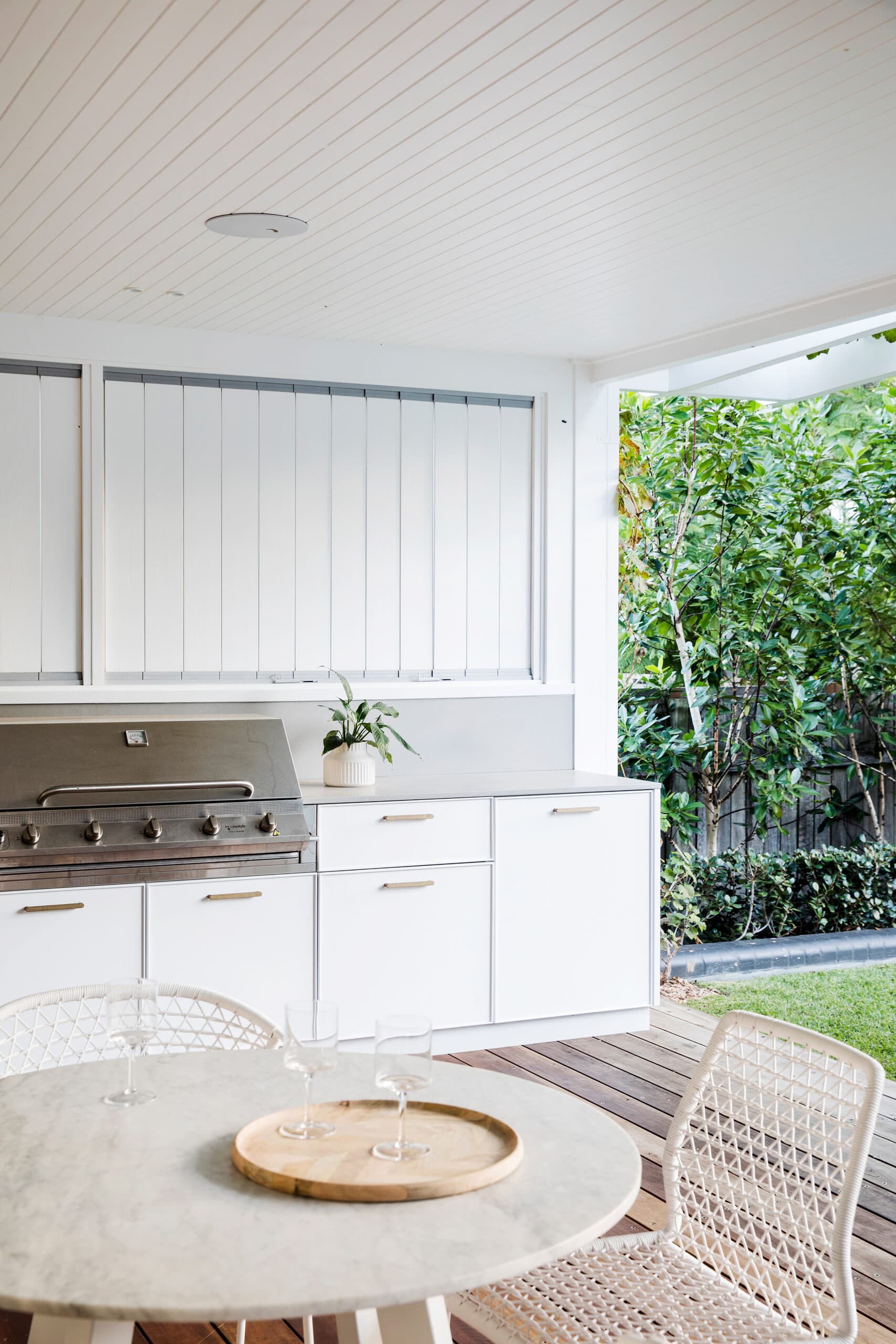 Outdoor kitchen with stainless barbecue, white joinery and a round marble table