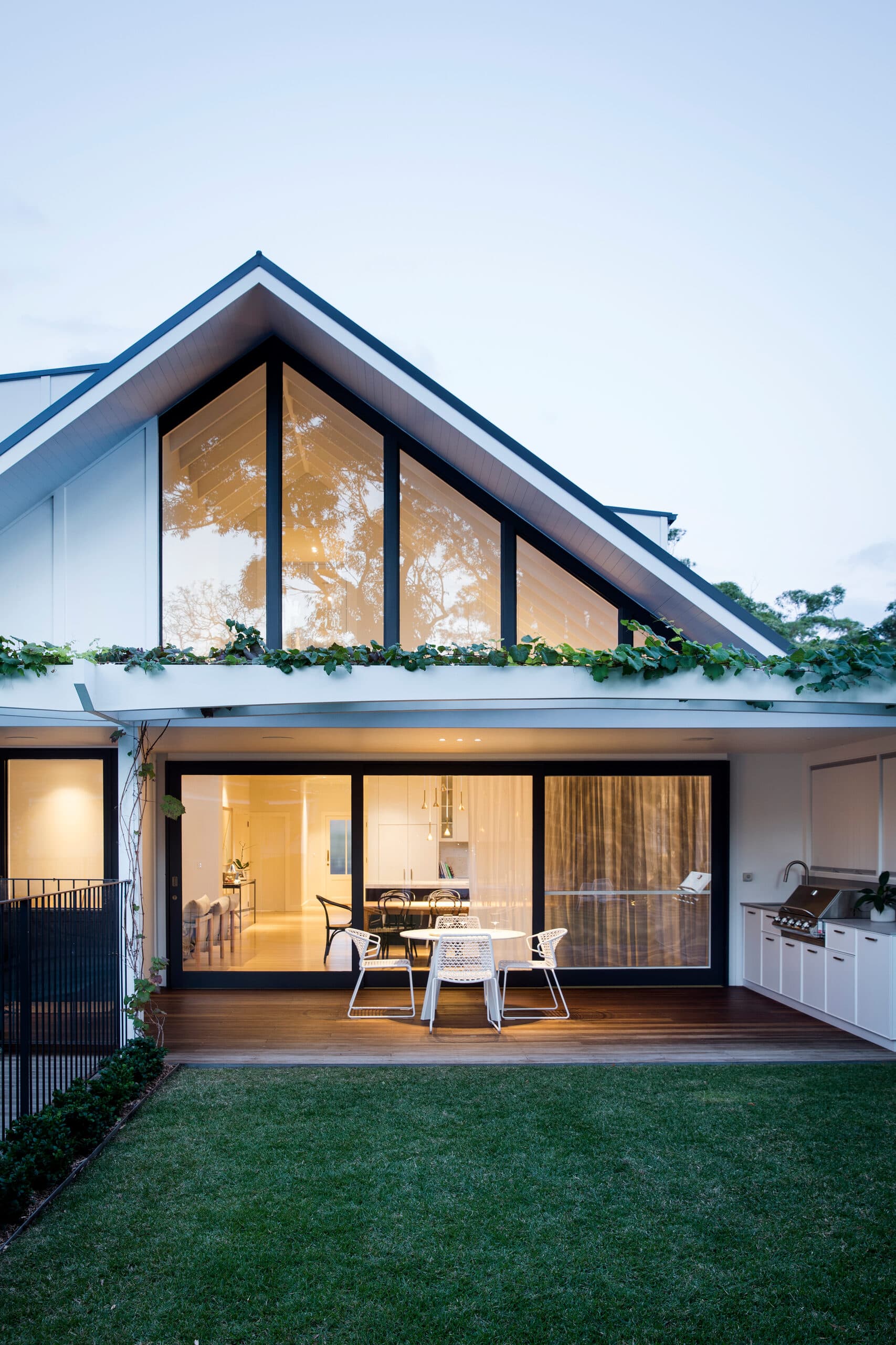 Glazed gable home at dusk with open sliding doors, deck dining and lawn