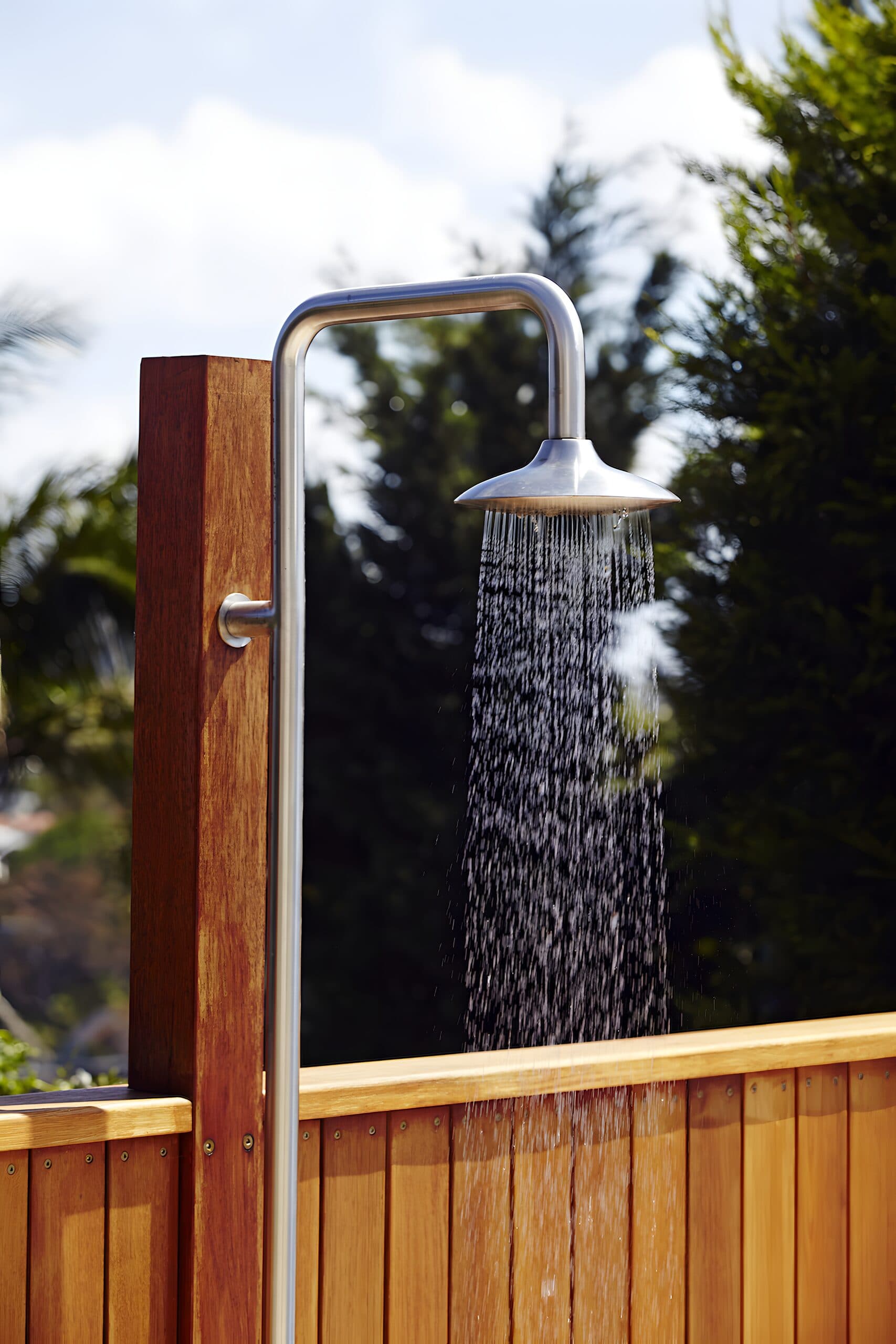 Stainless steel outdoor shower running against a timber slat privacy screen