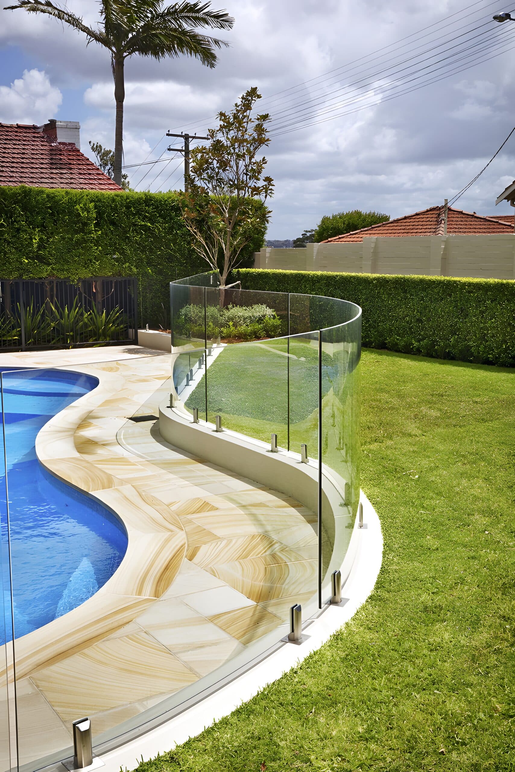 Curved frameless glass fence tracing the sandstone pool coping above a level lawn
