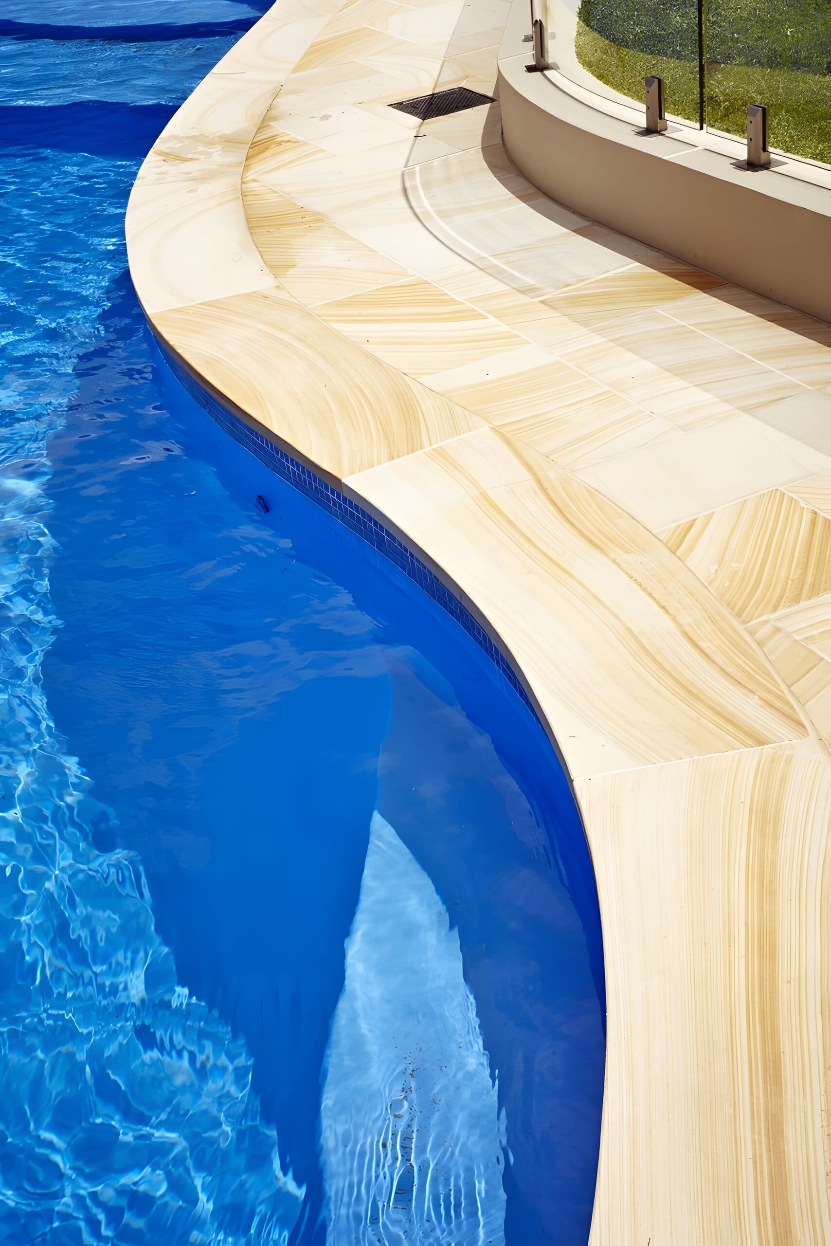 Overhead view of pale sandstone coping curving along the edge of the deep blue pool