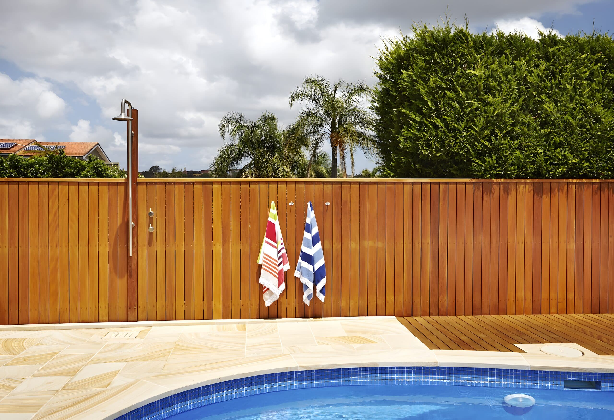 Two striped beach towels hanging on the timber fence beside an outdoor shower and the pool edge