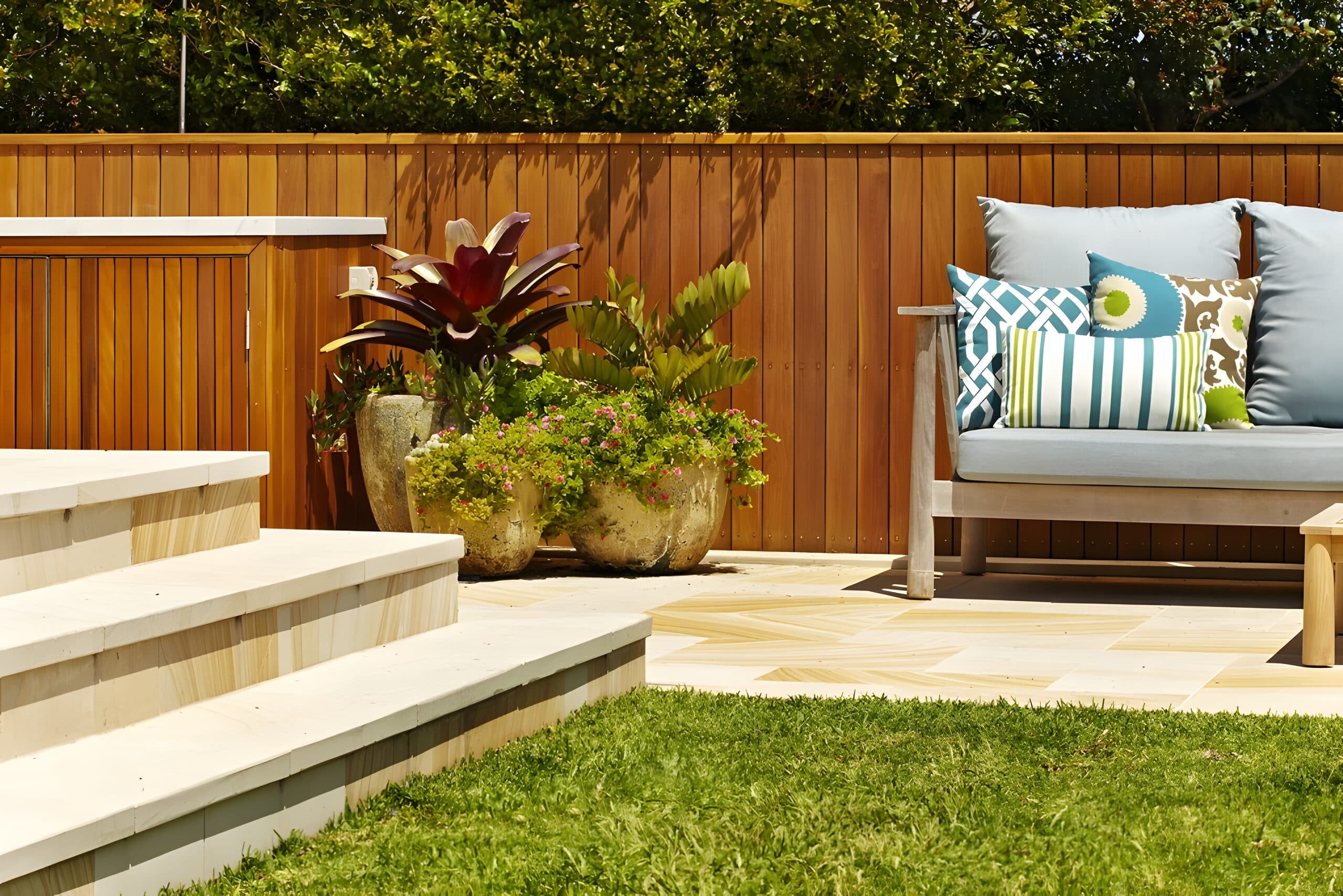 Sandstone steps beside a cluster of planted stone pots and a timber lounge with patterned cushions