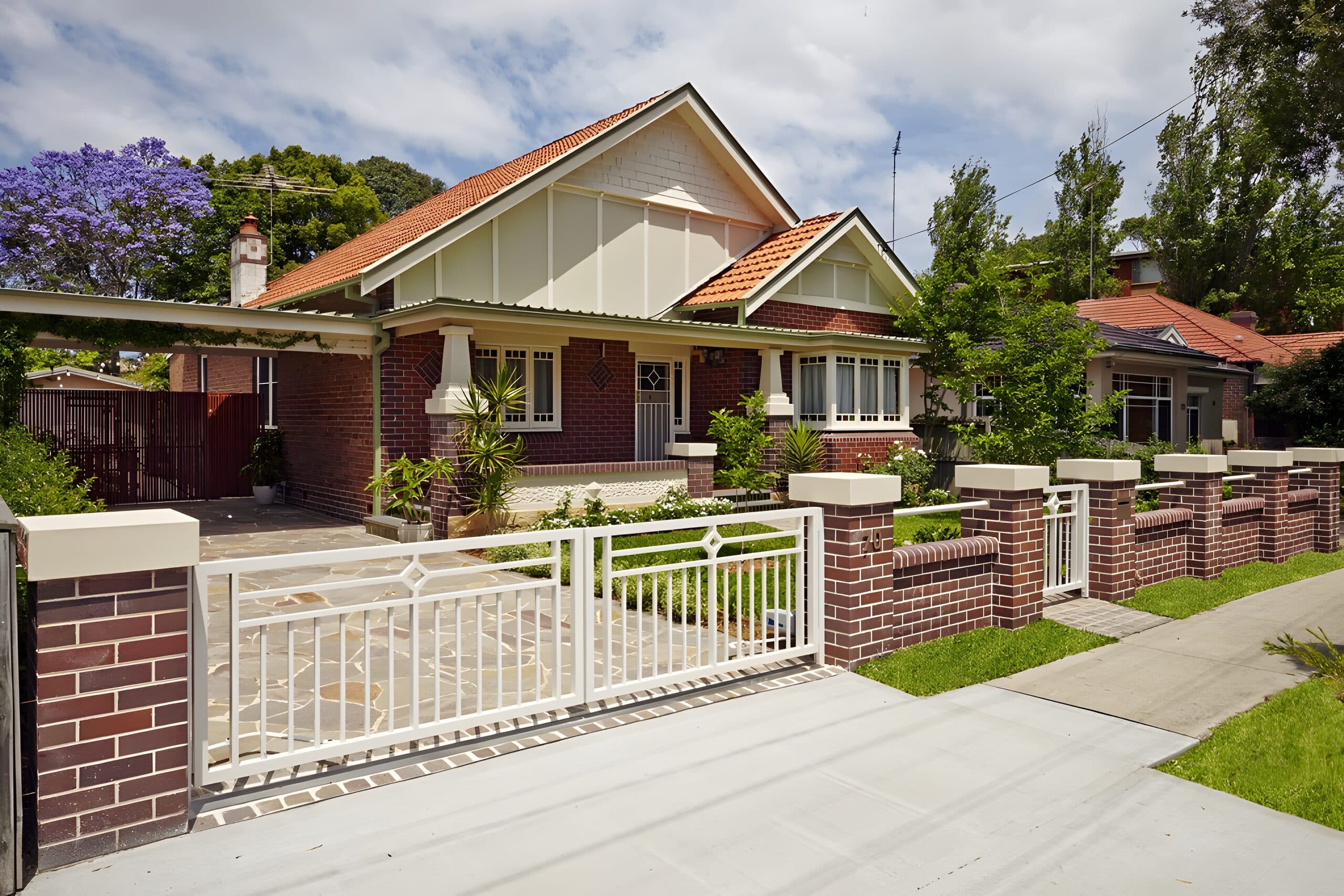 Restored Federation brick bungalow behind a red-brick fence and white steel gate with a crazy-paved driveway