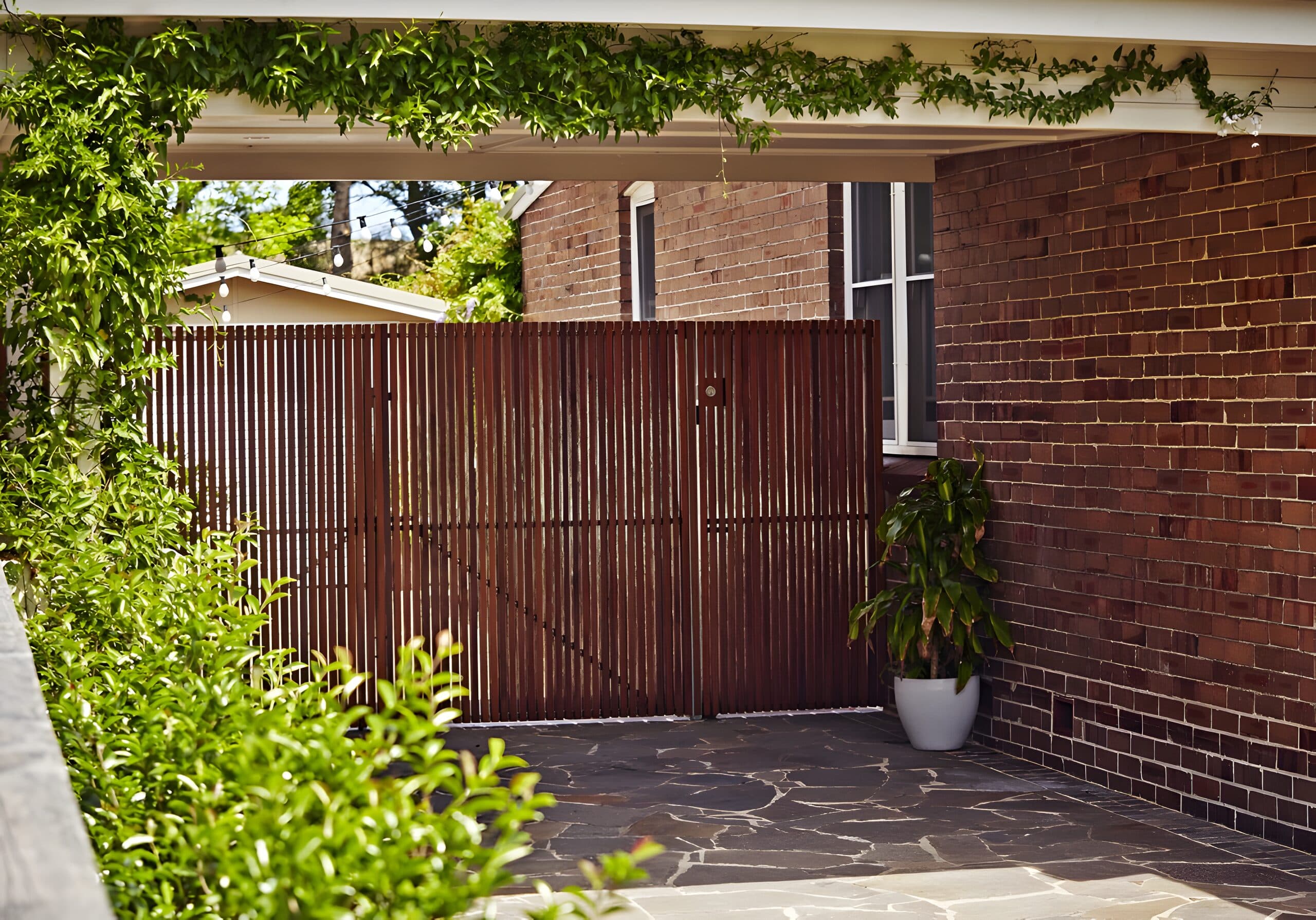 Jasmine-clad carport entry with a timber slat gate and crazy-paved stone floor