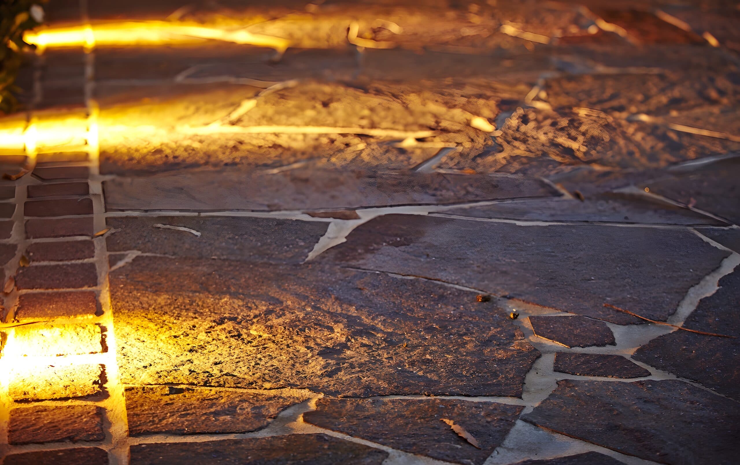 Crazy-paved stone washed by a warm strip of garden lighting at dusk