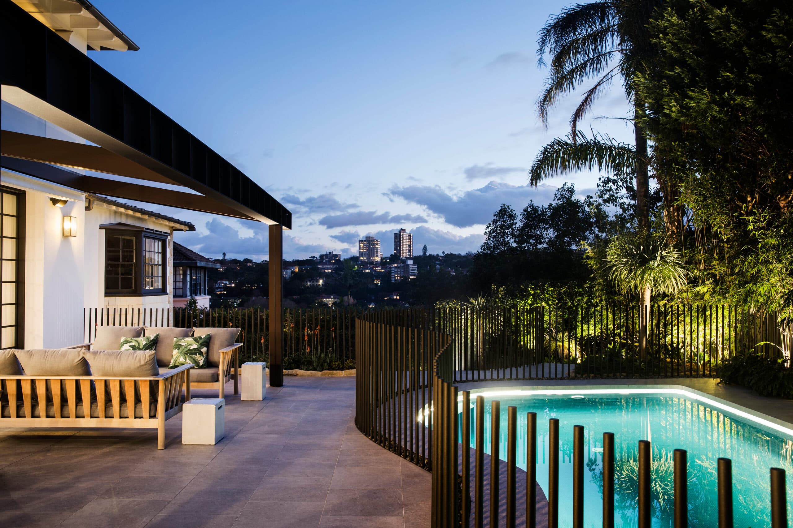 Pool terrace at dusk beside the house with distant city skyline under a deep blue sky