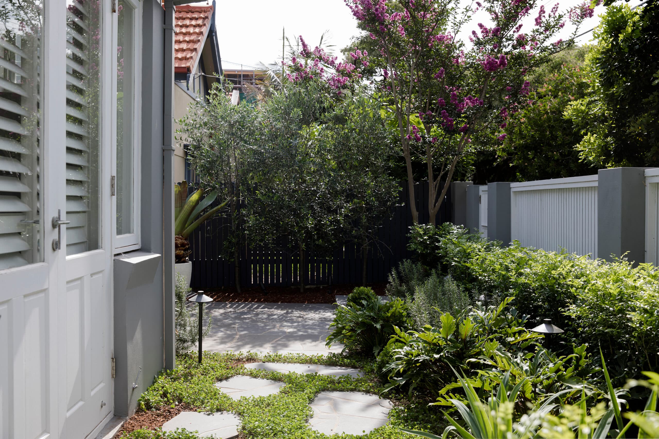 Side path of flagstone steppers beside white timber doors leading to a black picket gate