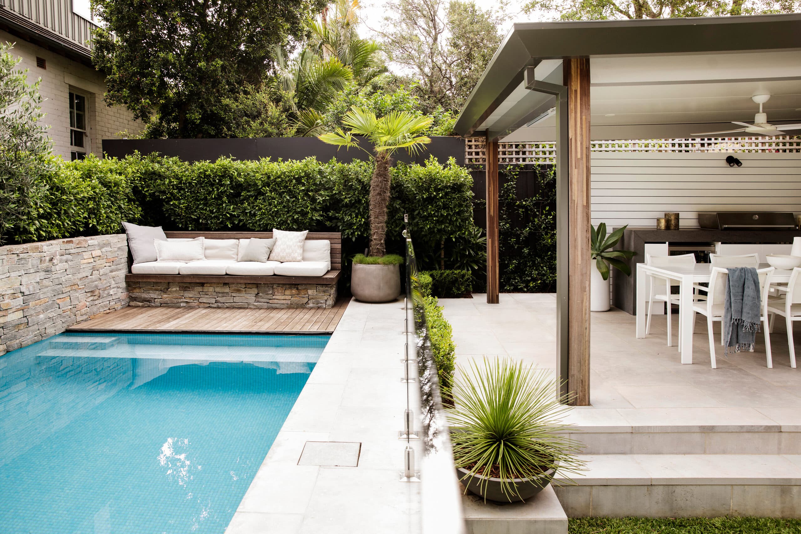 Elevated view across the mosaic pool to a stone-clad daybed and covered alfresco dining beyond