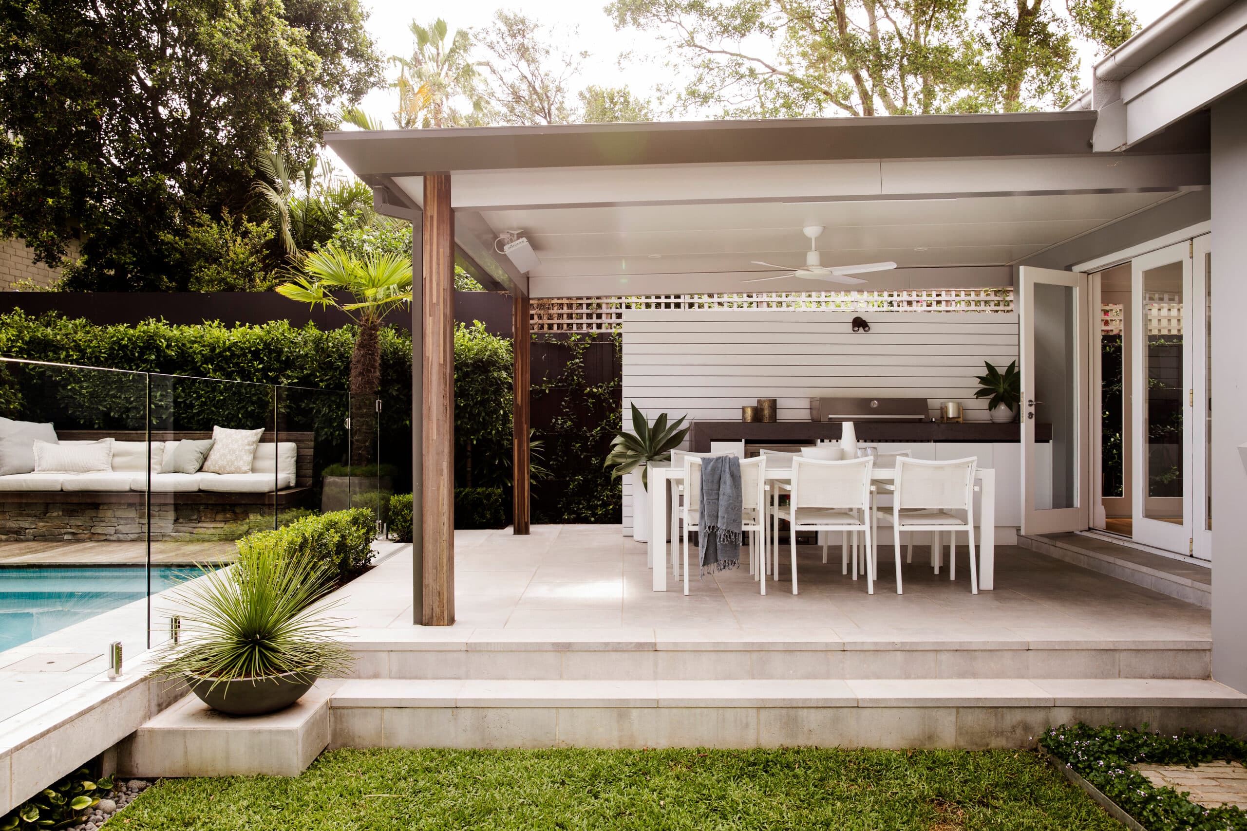 Covered alfresco with white dining setting and barbecue overlooking the pool and daybed