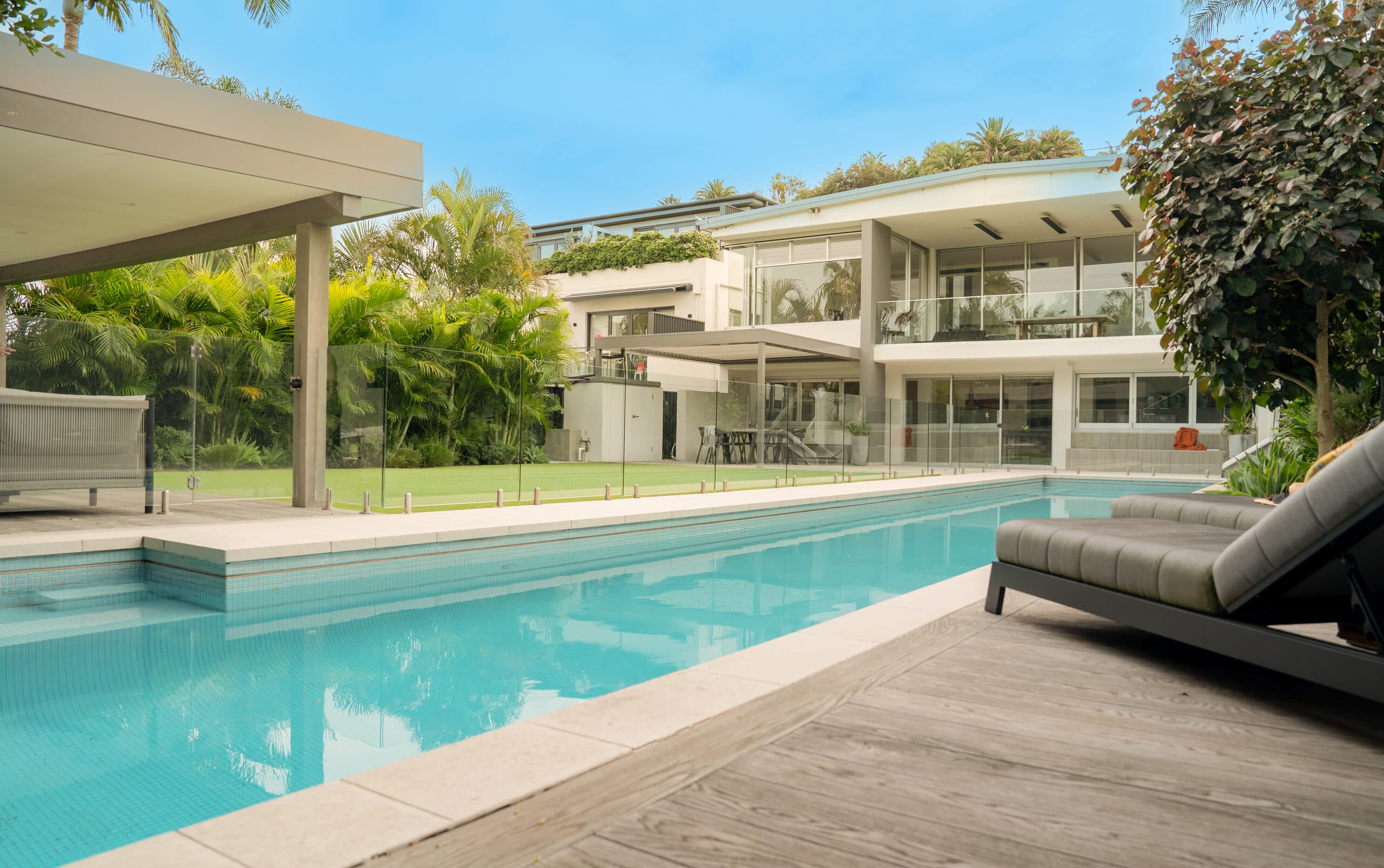 Long pool viewed from the timber-look deck toward the contemporary house