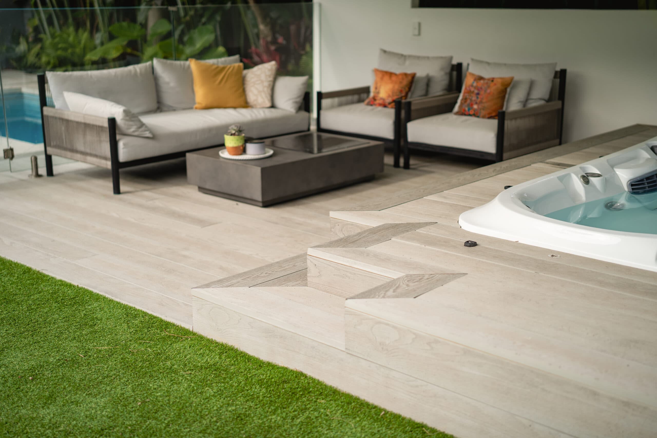 Cabana lounge and integrated spa beside pale paving and artificial lawn
