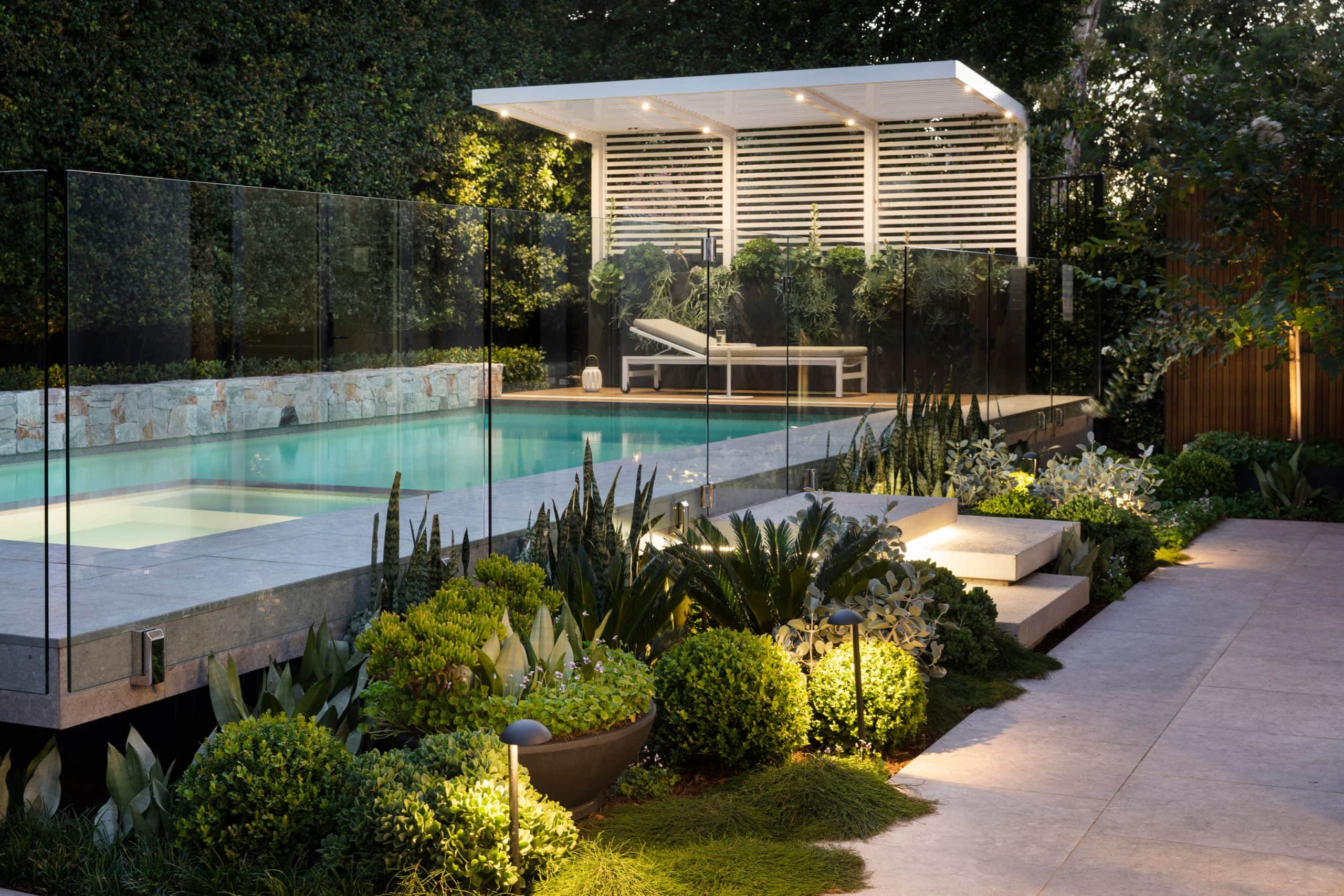 Maroubra Secluded Gem garden at dusk — illuminated floating pool, white slatted pergola and lush native planting, Eastern Suburbs Sydney